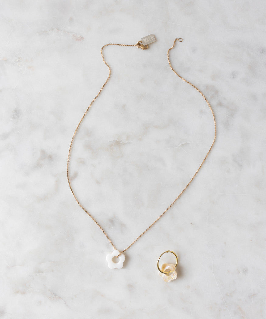 A stunning Mother of Pearl Flower Charm Set by WALD World, featuring a gold necklace with a white flower pendant and a matching gold ring adorned with real mother of pearl flowers, elegantly displayed on a white marble surface.