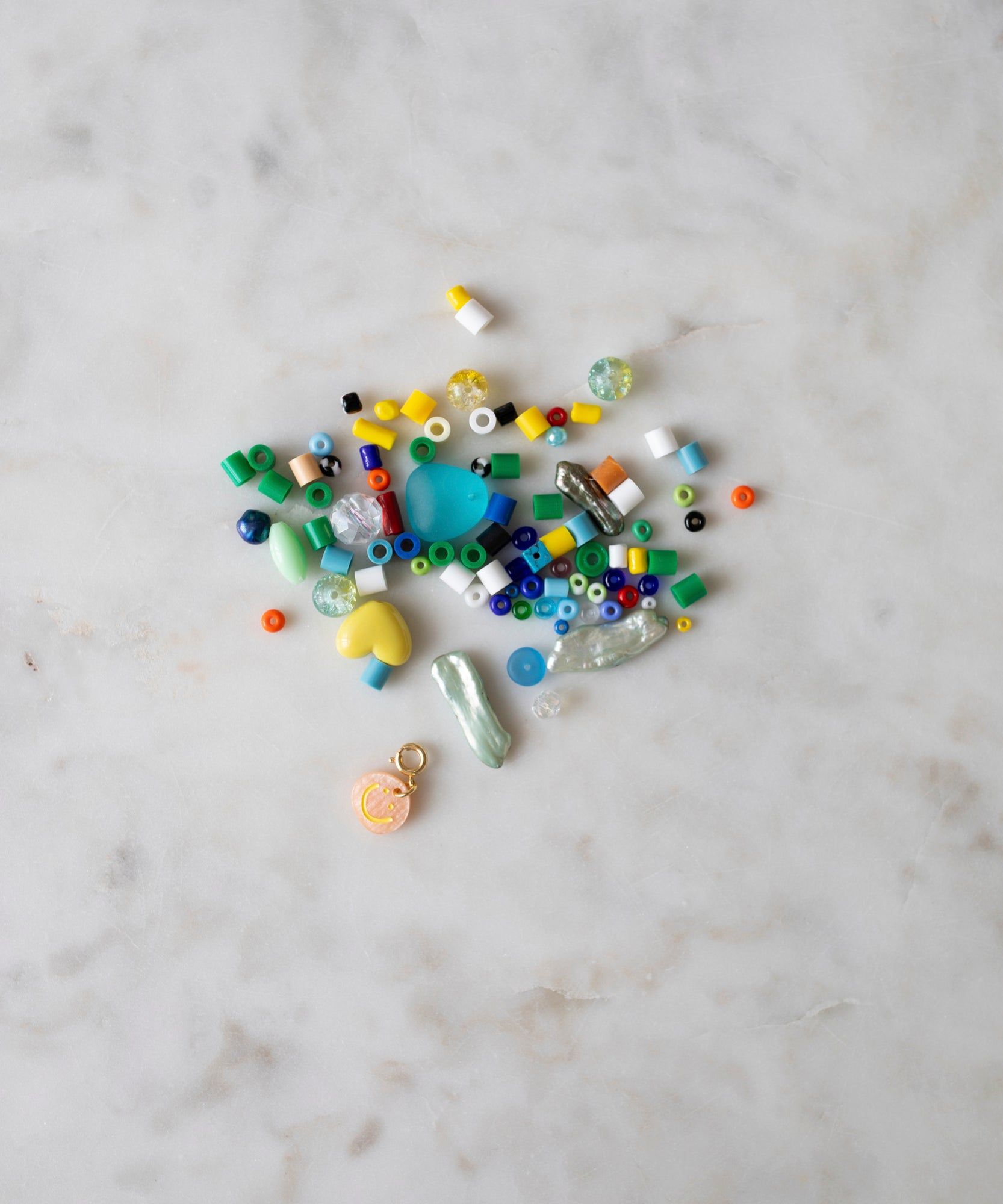 A collection of assorted colorful beads, pearls in various colorways, and craft materials scattered on a marble surface for creating a WALD Berlin Candyman Necklace + Bracelet Kit.