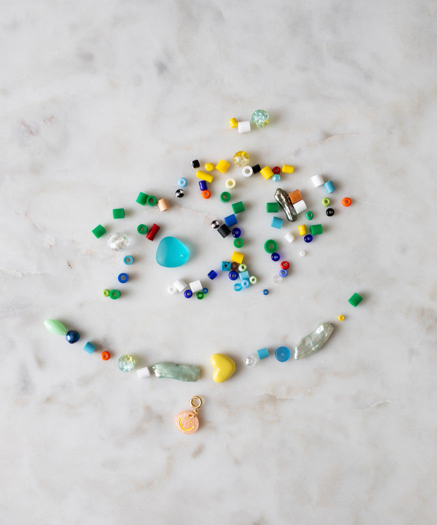 Assorted beads, pearls in a colorway, and small trinkets scattered on a marble surface were replaced with the Candyman Necklace + Bracelet Kit by WALD Berlin.