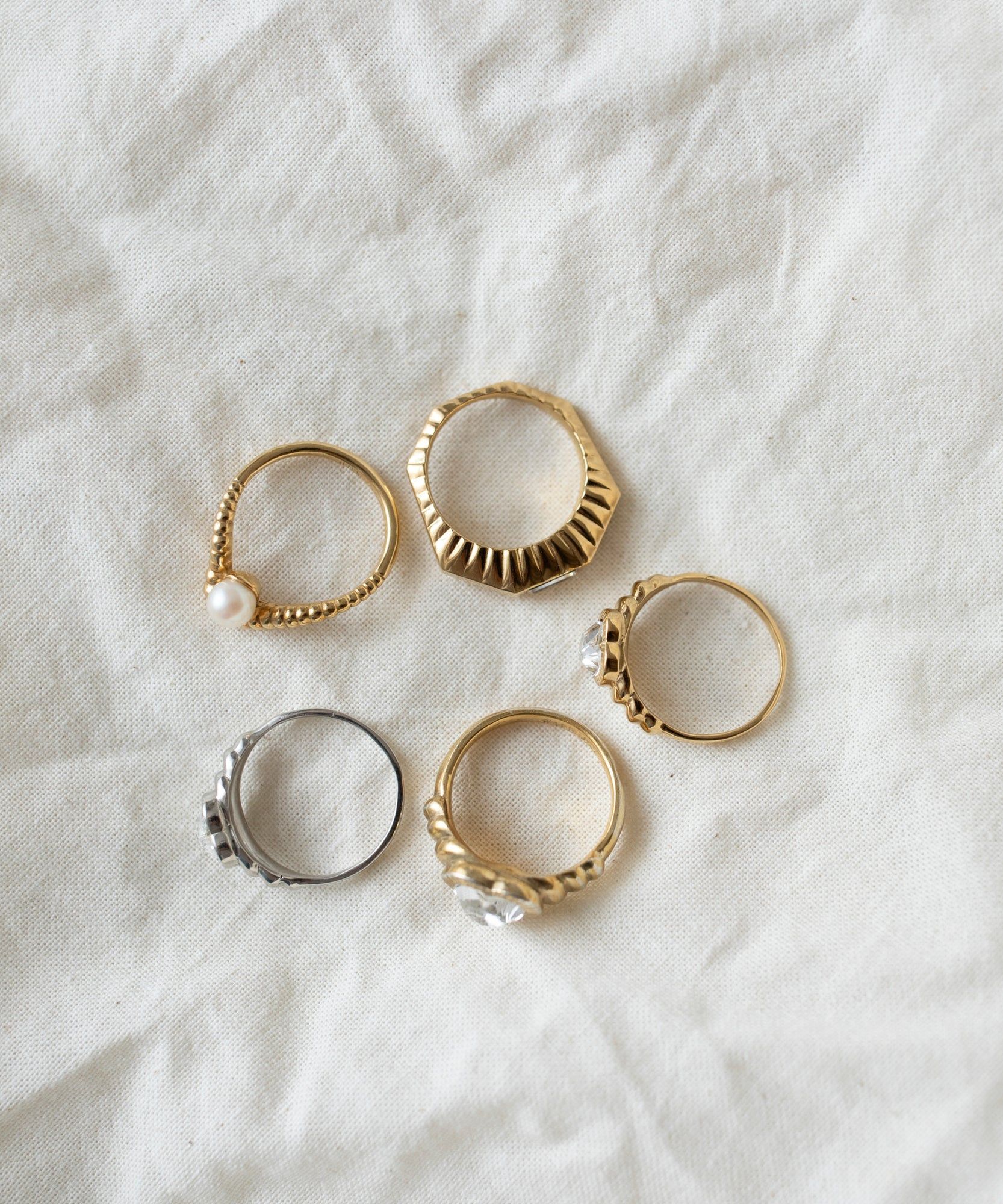 Assorted rings, including a WALD Berlin Be My Lover Ring Mini, on a textured fabric surface.