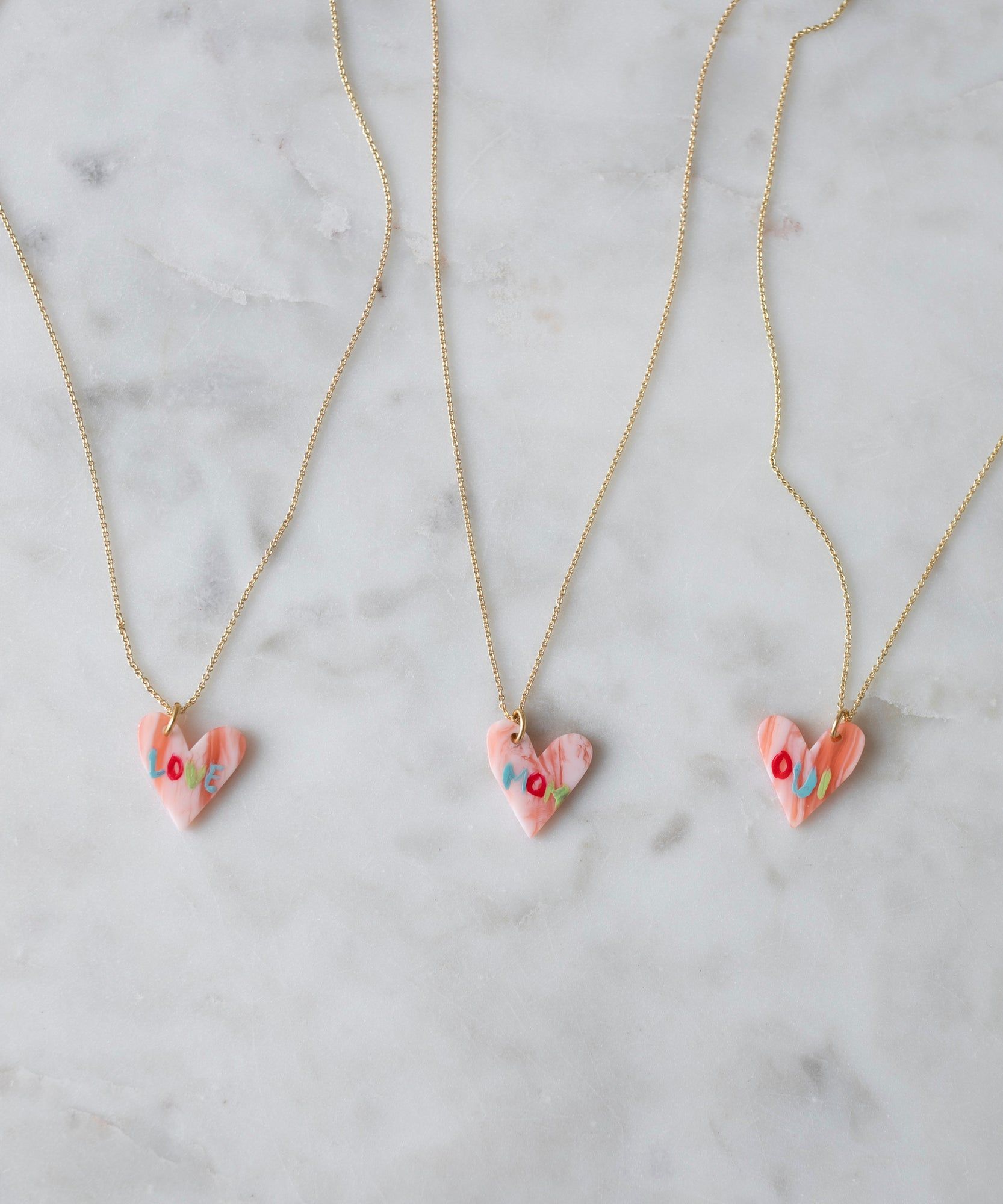 Three Pledges Of Tenderness MOM Necklaces with floral patterns on a marble surface by WALD Berlin.