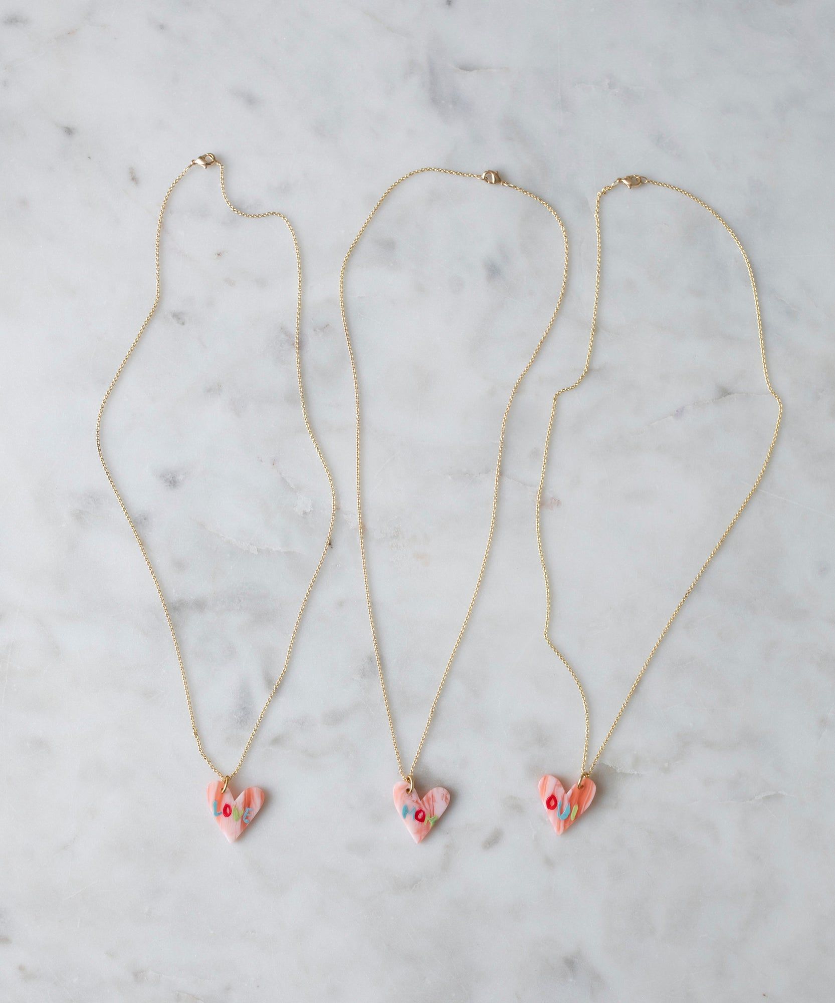 Three Pledges Of Tenderness LOVE Necklaces by WALD Berlin with eye motifs, made in Germany, displayed on a marble surface.