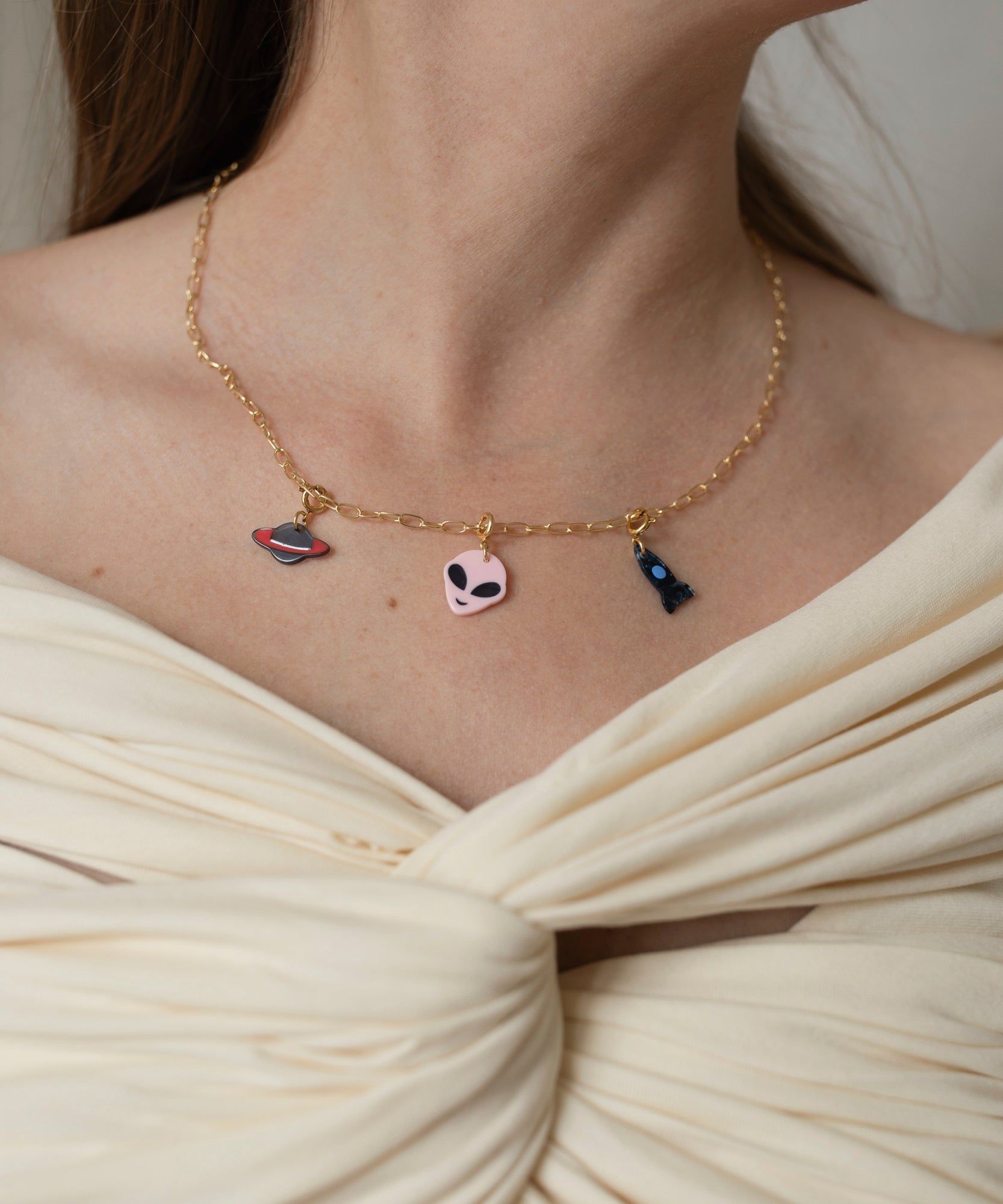 Close-up of a woman wearing a WALD Berlin Alien Dark Necklace with colorful charms, including a heart and a mask, against a cream top.