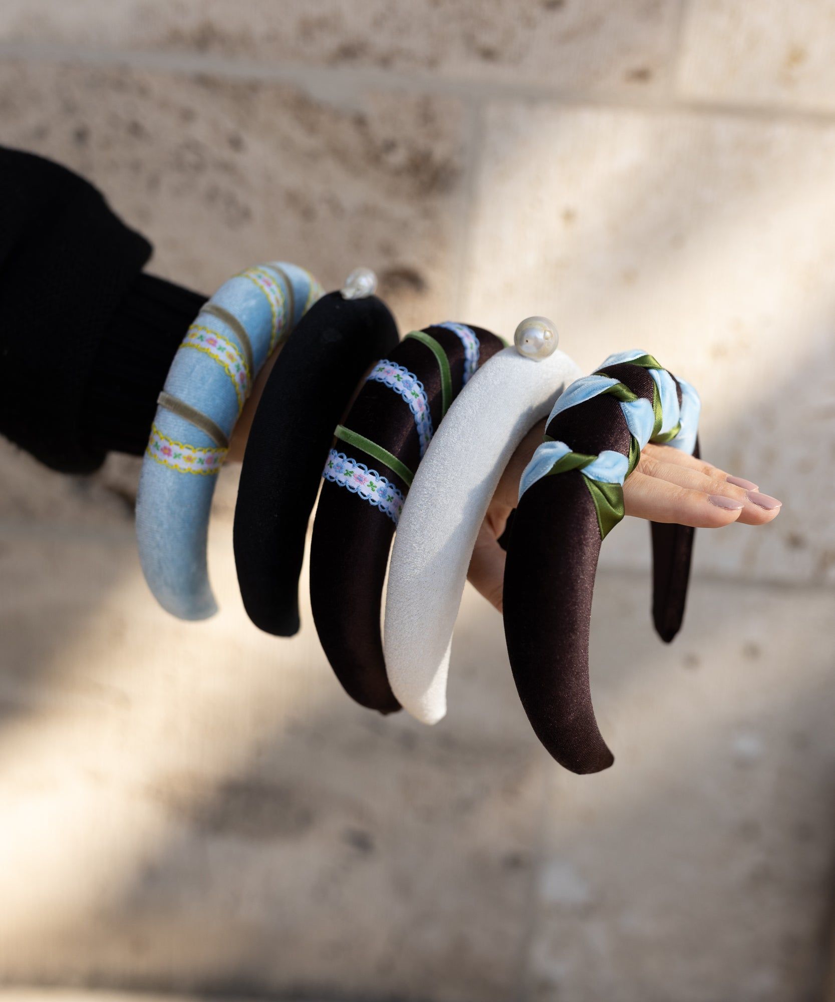 A woman's hand holding a bunch of WALD Berlin Headband Swirl Light Blue bracelets.