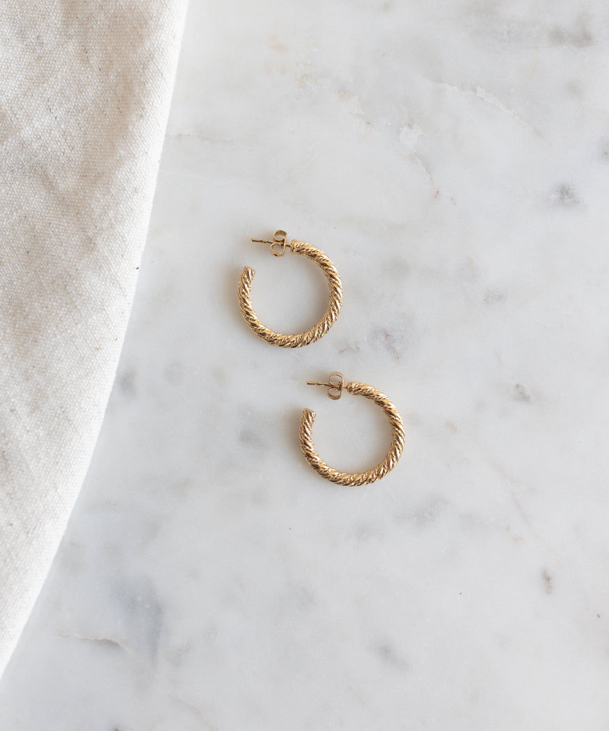 A pair of Linda Earrings Gold by WALD Berlin hoop earrings on a marble table.