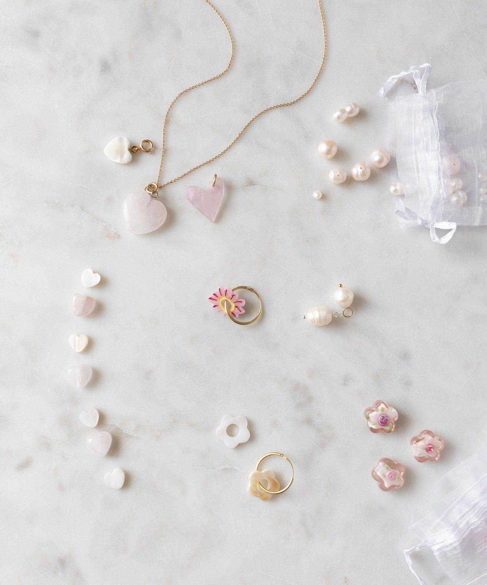 Assorted jewelry, including heart-shaped pendants, rings, pearl earrings, and the WALD World Mother of Pearl Heart Beads Set, are spread out on a marble surface. A small sheer bag contains additional WALD World mother of pearl necklaces and other jewelry items.