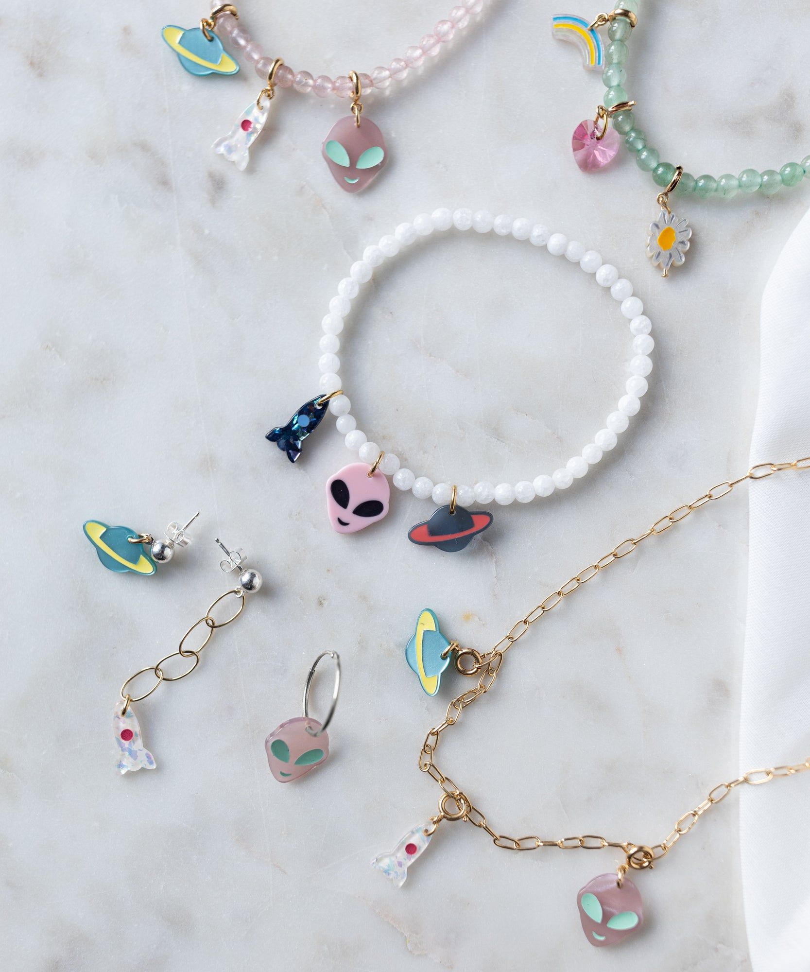 A collection of From Another Mother Rosé Orbit Bracelets and necklaces with aliens on them, inspired by the beauty of rose quartz stones, designed and crafted in Germany by WALD Berlin.
