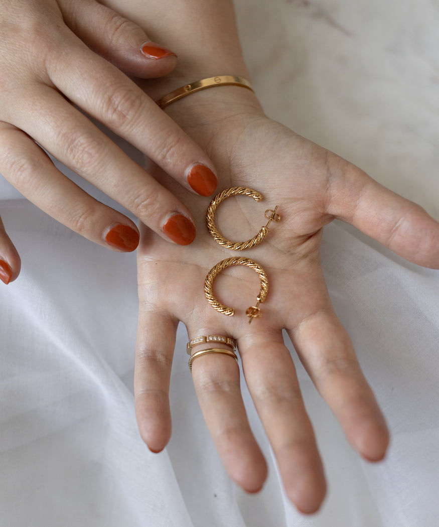 A person's hands displaying WALD Berlin Linda Earrings Gold, sterling silver earrings, and painted nails against a white fabric background.