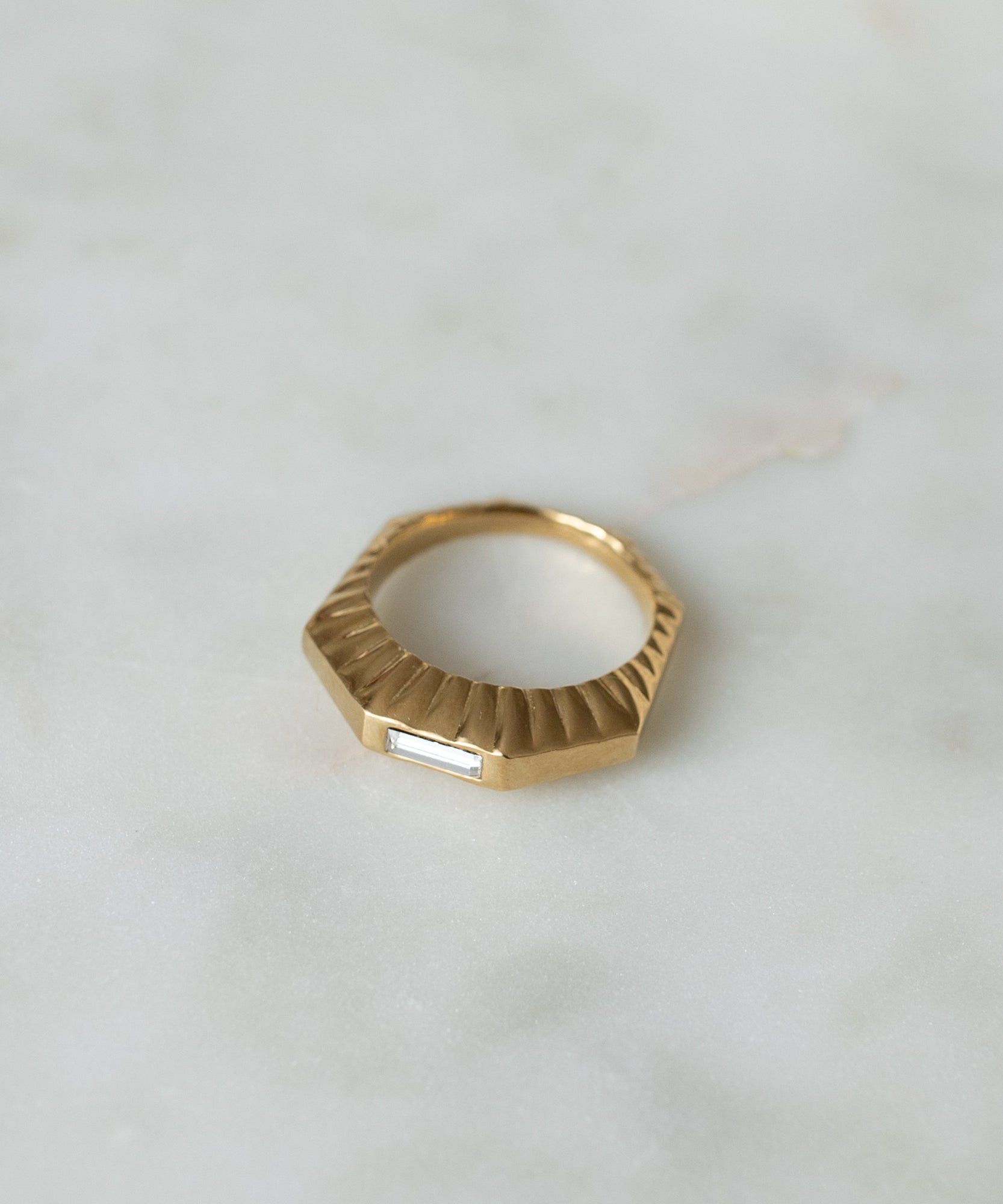 WALD Berlin Shining Star Gold Ring with a textured surface and a single rectangular gemstone, resting on a marble surface.