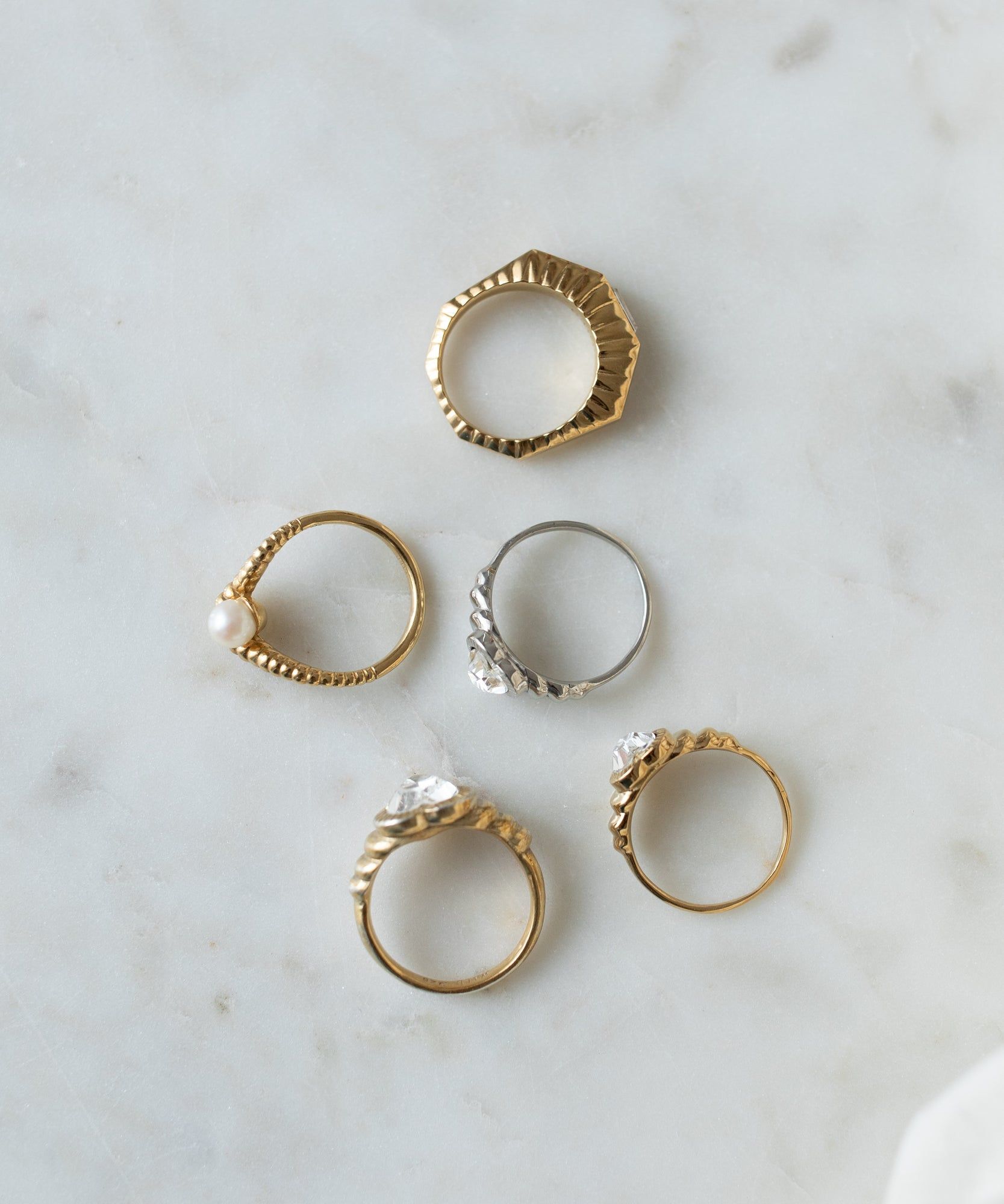 Six assorted Shining Star Gold Rings, including pearl and Swarovski stone designs, arranged on a marble surface by WALD Berlin.