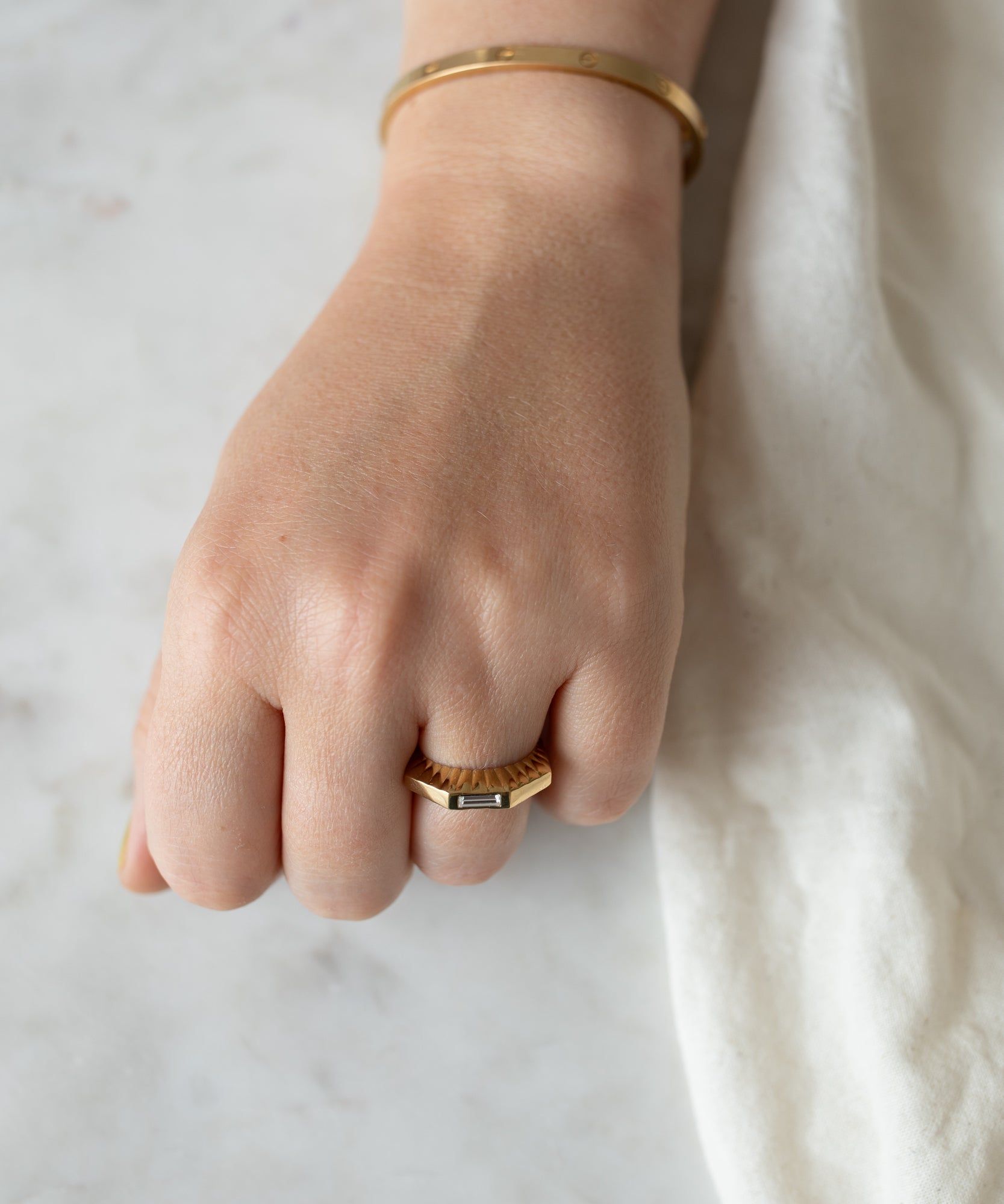 A close-up of a woman's hand resting on a marble surface, wearing a WALD Berlin Shining Star Gold Ring and bracelet.