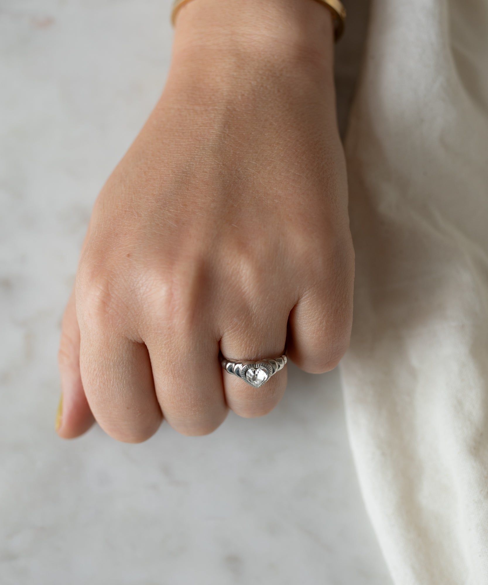Close-up of a woman's clenched fist resting on a marble surface, showcasing a WALD Berlin Be My Lover Mini Silver Ring with a large round gemstone.