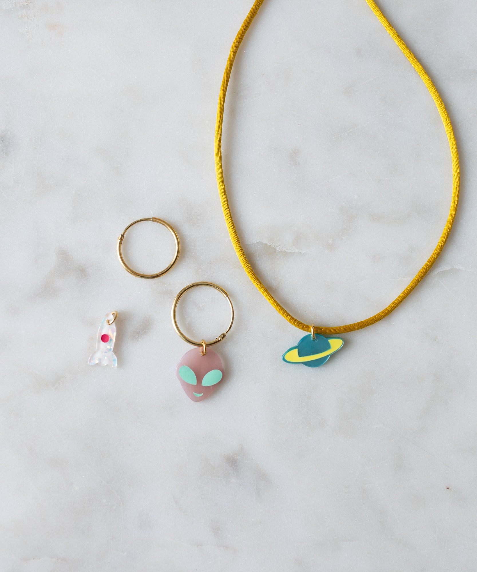 Rocket Charm necklace and matching earrings with colorful, abstract pendants on a marble surface crafted as DIY jewelry by WALD World.