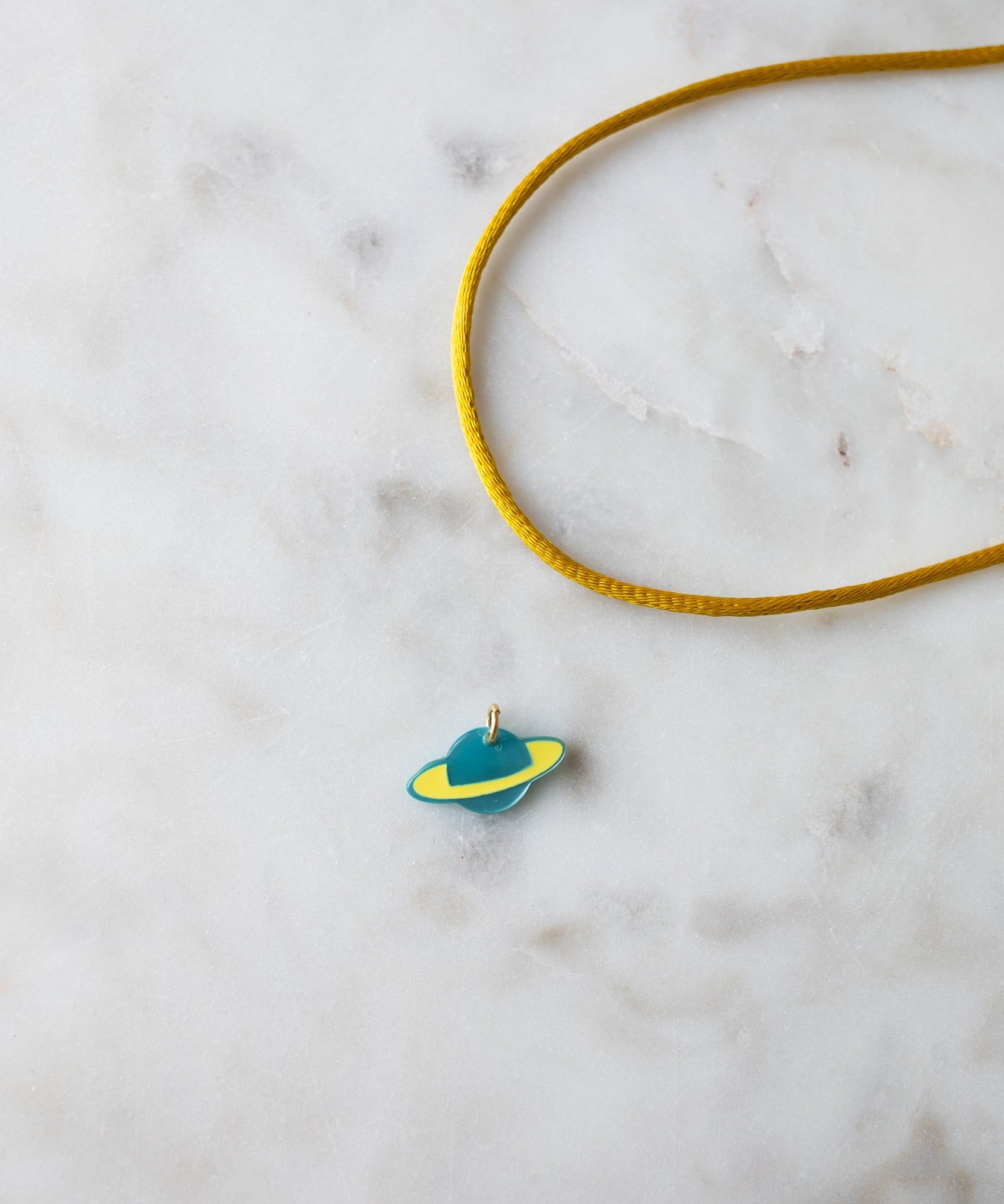 A Venus Charm pendant from WALD World on a yellow cord lying on a marble surface.