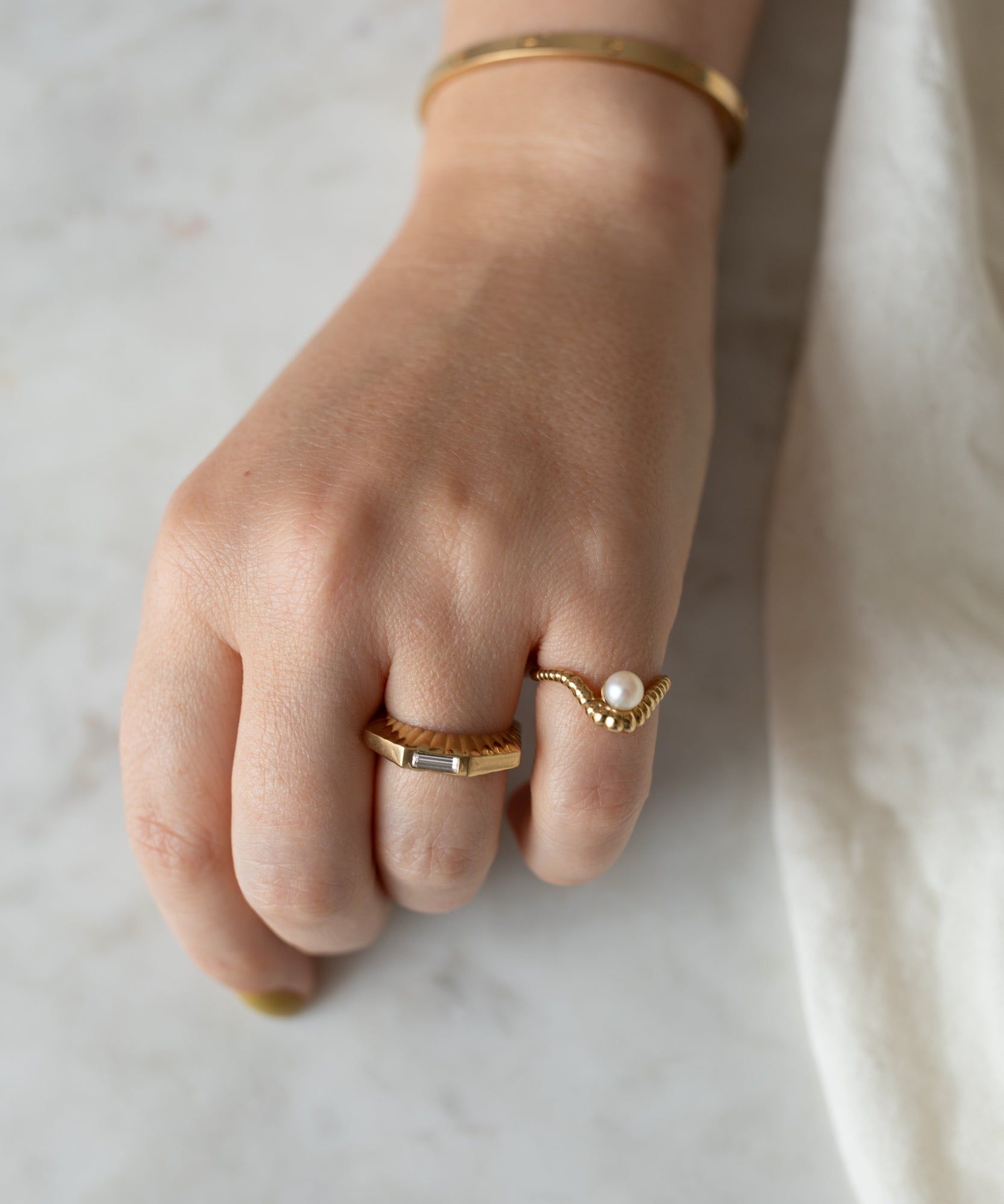 A woman's hand resting on a marble surface, adorned with three WALD Berlin Shining Star Gold Rings, against a soft white background.