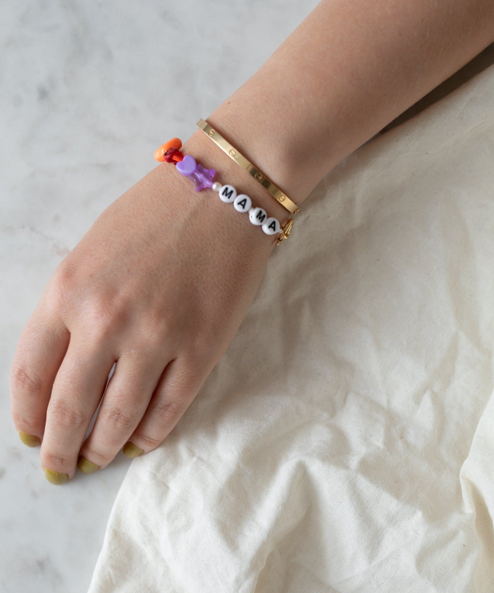 A person's wrist adorned with colorful handmade jewelry, including one with letter beads spelling 