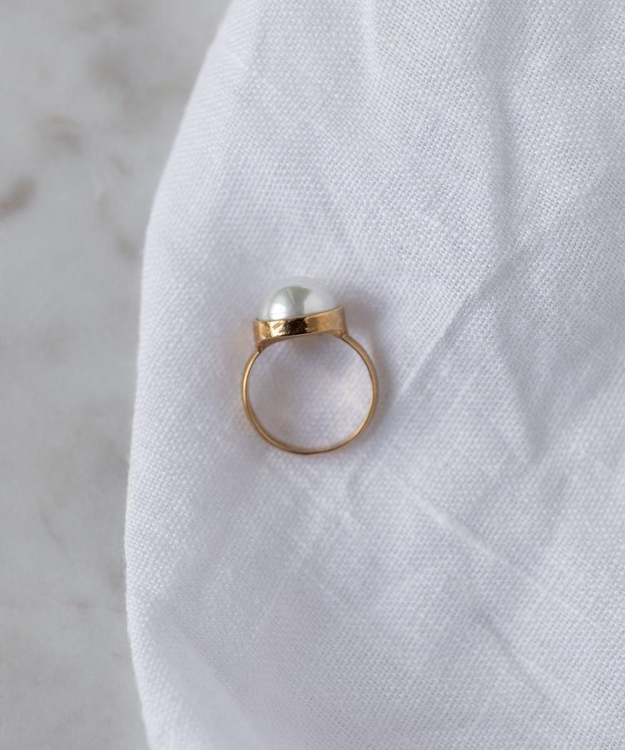 The WALD Berlin Pop Pearl Ring, featuring a single pearl set in 18k gold plated brass, rests on white fabric, blending modern style with timeless elegance.