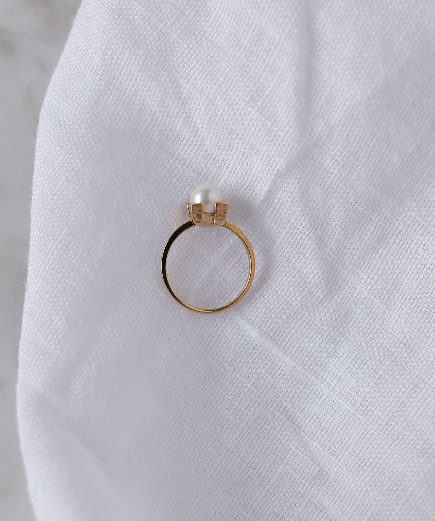 The WALD Berlin Pop Pearl Ring Mini, crafted in 18k gold plated brass, sits on white textured fabric, blending modern flair with classic elegance.