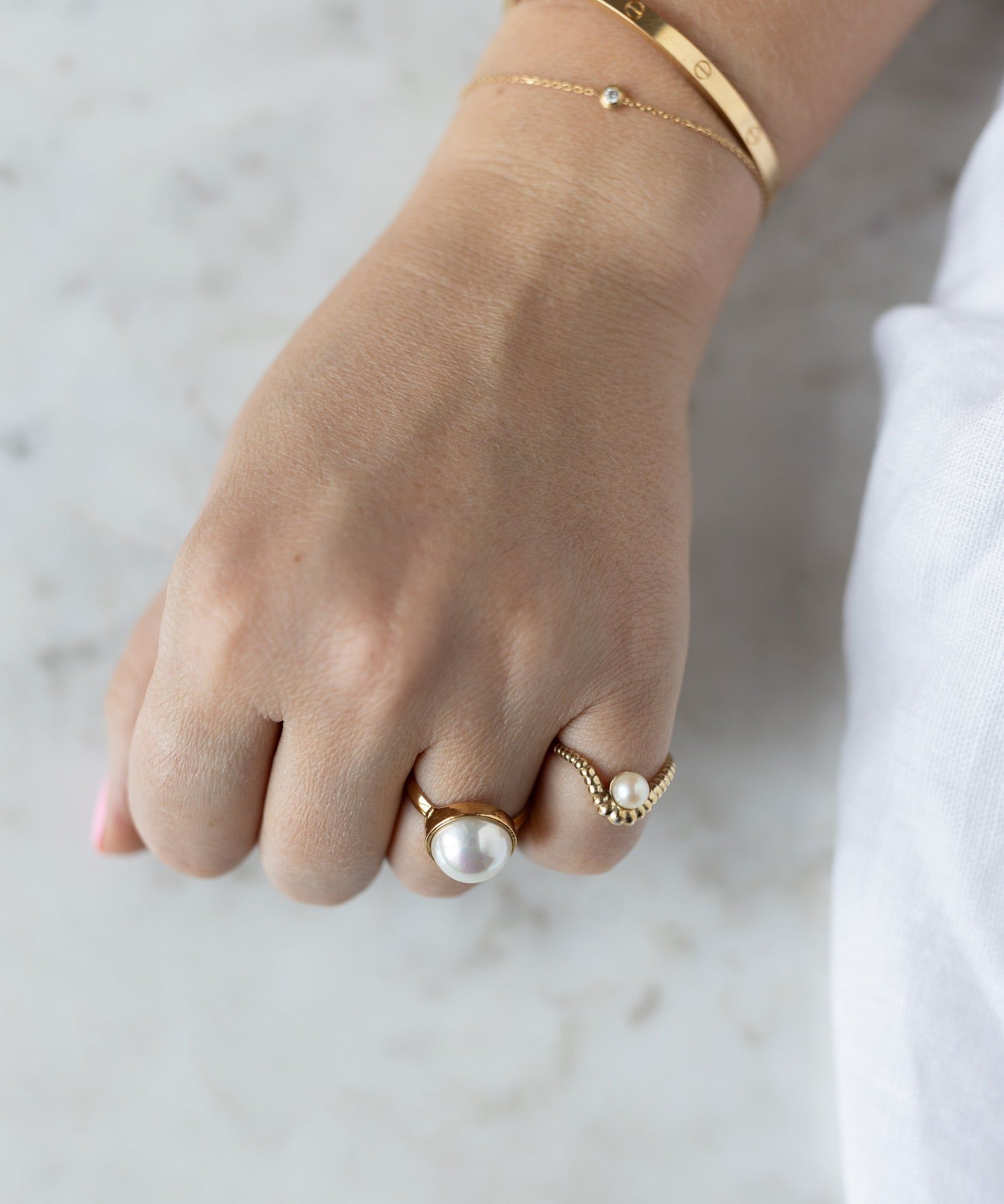 A hand adorned with two WALD Berlin Pop Pearl Rings and a gold bracelet, all in 18k gold plated brass, rests on a light surface for a modern touch.