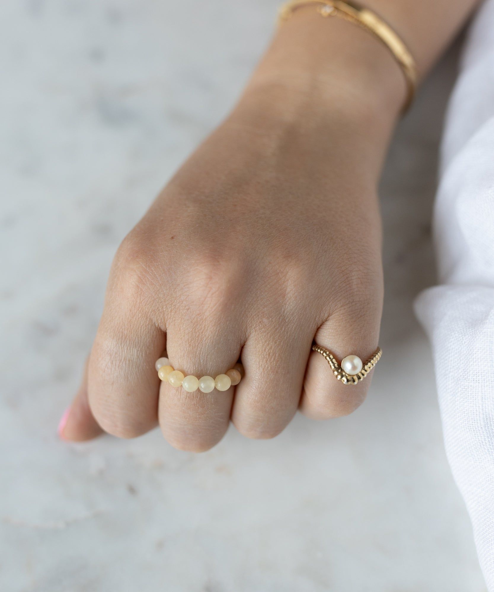 A hand wearing WALD Berlin's Pop Gemstone Ring Set, featuring vibrant rings and a gold bracelet—chic gift ideas with adjustable sizing for the perfect fit.