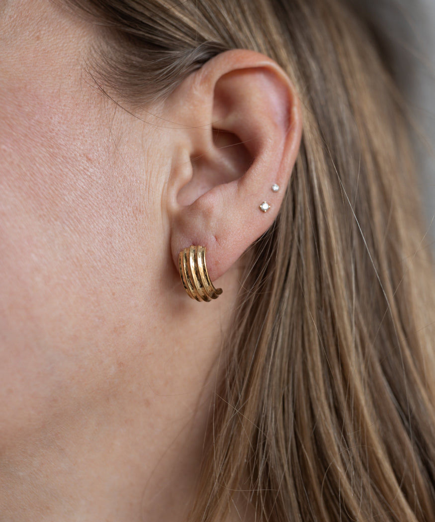 Close-up of a person’s ear with long blonde hair, wearing WALD Berlin's Pop Wave Earrings Small—an 18k gold plated creole hoop in the lobe and two small 925 silver pin studs in the upper ear.