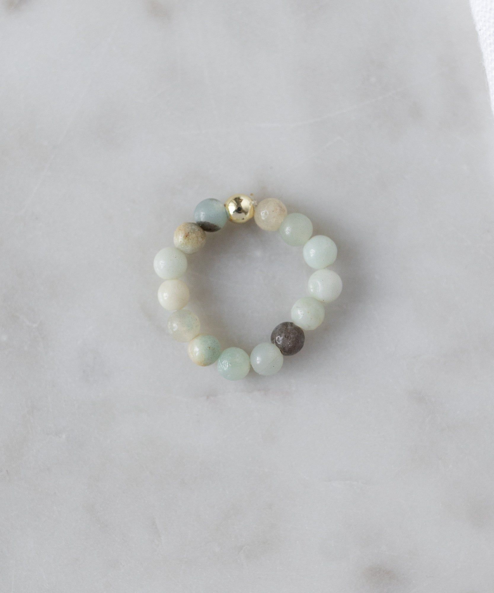 The WALD Berlin Pop Gemstone Ring Set features light green and beige beads with a shiny gold accent and flexible sizing, shown on a white marble surface.