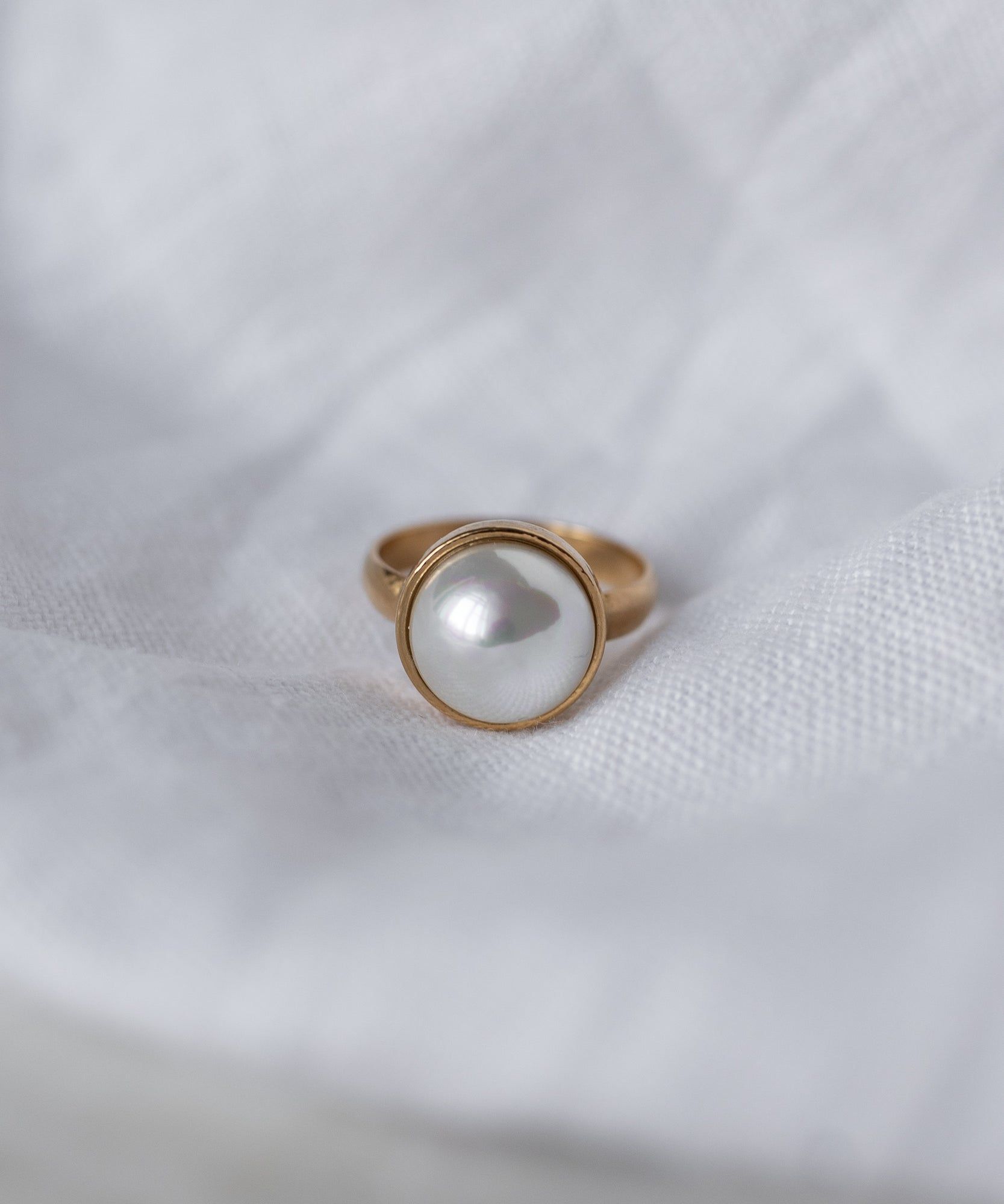 The WALD Berlin Pop Pearl Ring features a large round white pearl set in 18k gold plated brass, shown on a white textured fabric for a modern look.