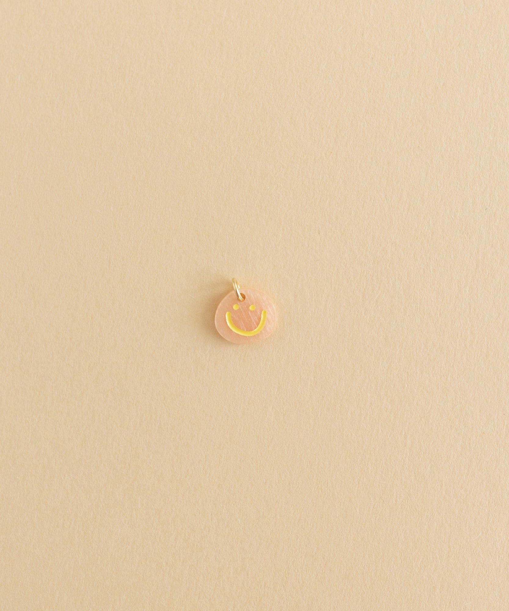 A small Smilie Dude Charm Orange jewelry by WALD World on a beige surface.