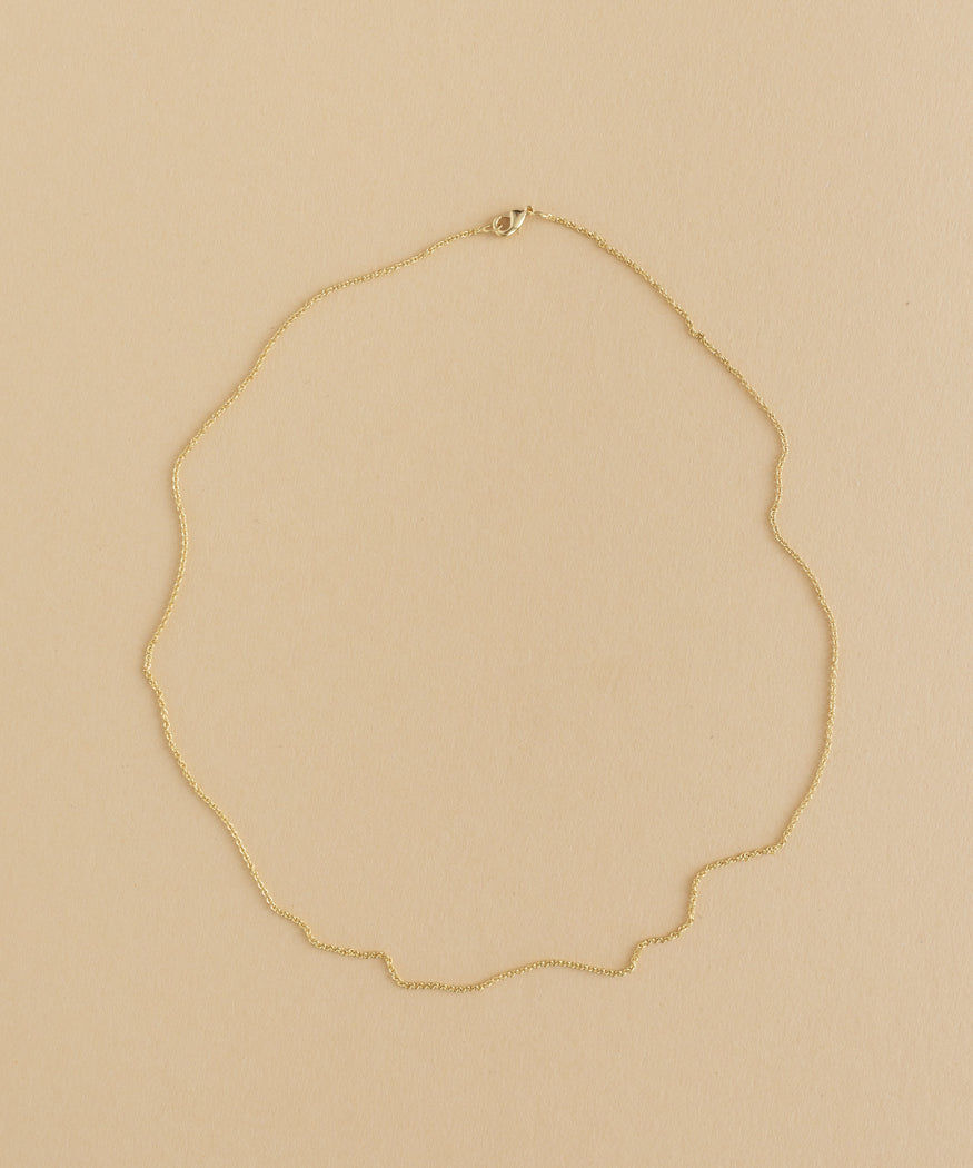 A gold necklace with a charm pendant on a beige background.