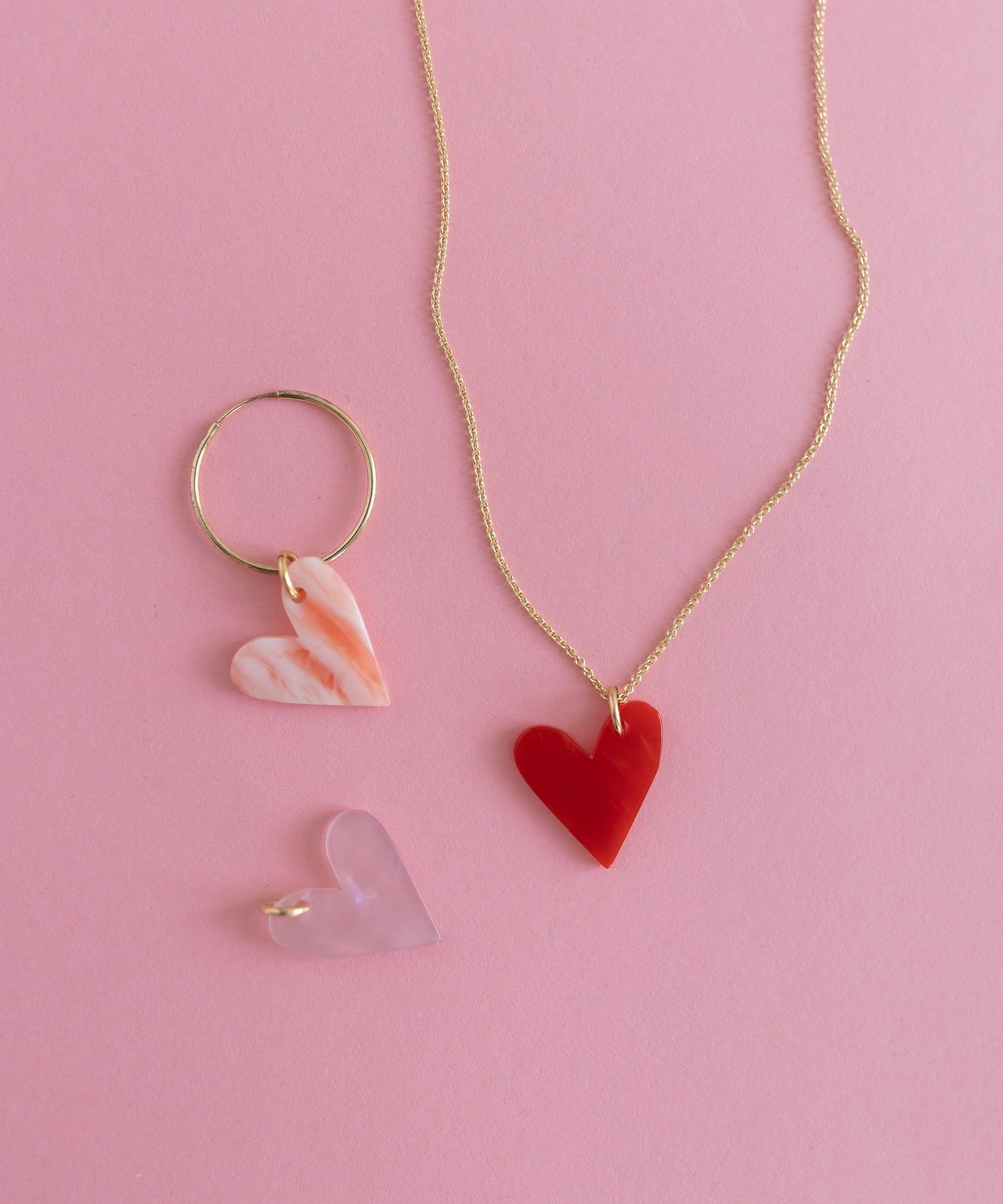 A WALD World gold heart shaped necklace and ring jewelry set on a pink background.