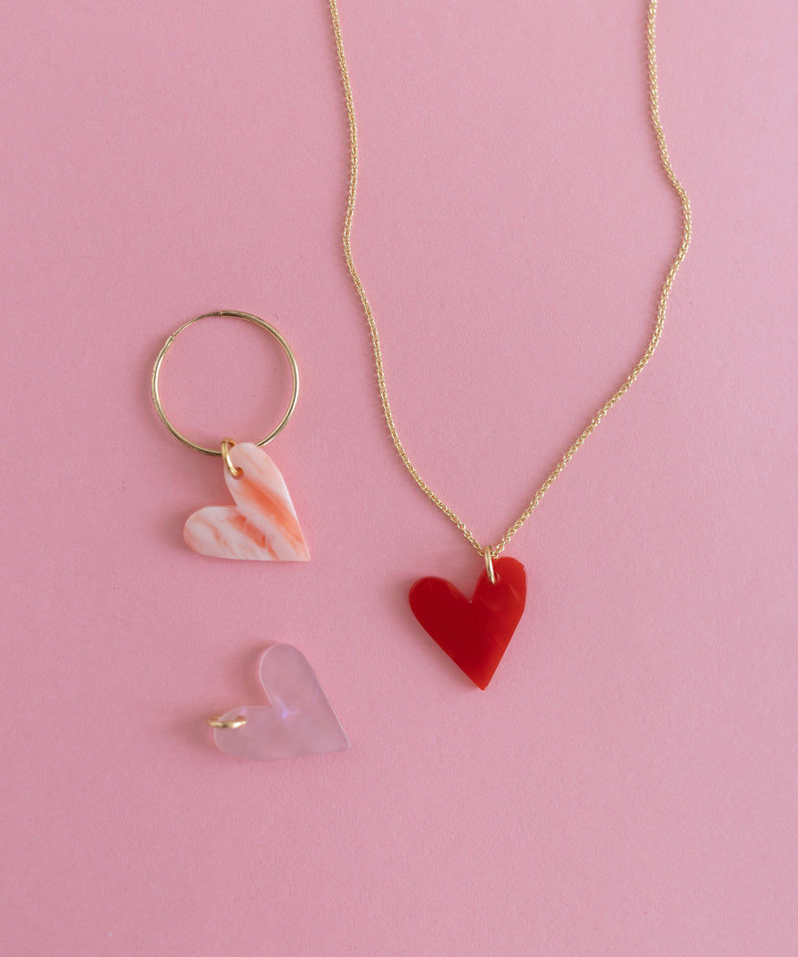 A DIY jewelry set, consisting of a necklace and ring with a purple Heart Charm, showcased on a pink background from WALD World.