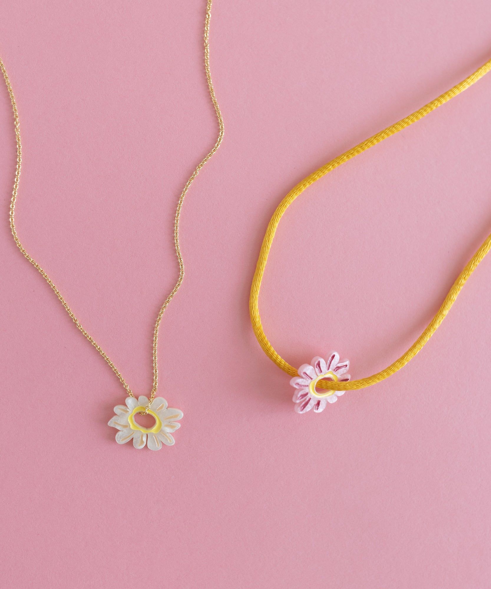 Two Daisy Charm Rose necklaces on a pink background.