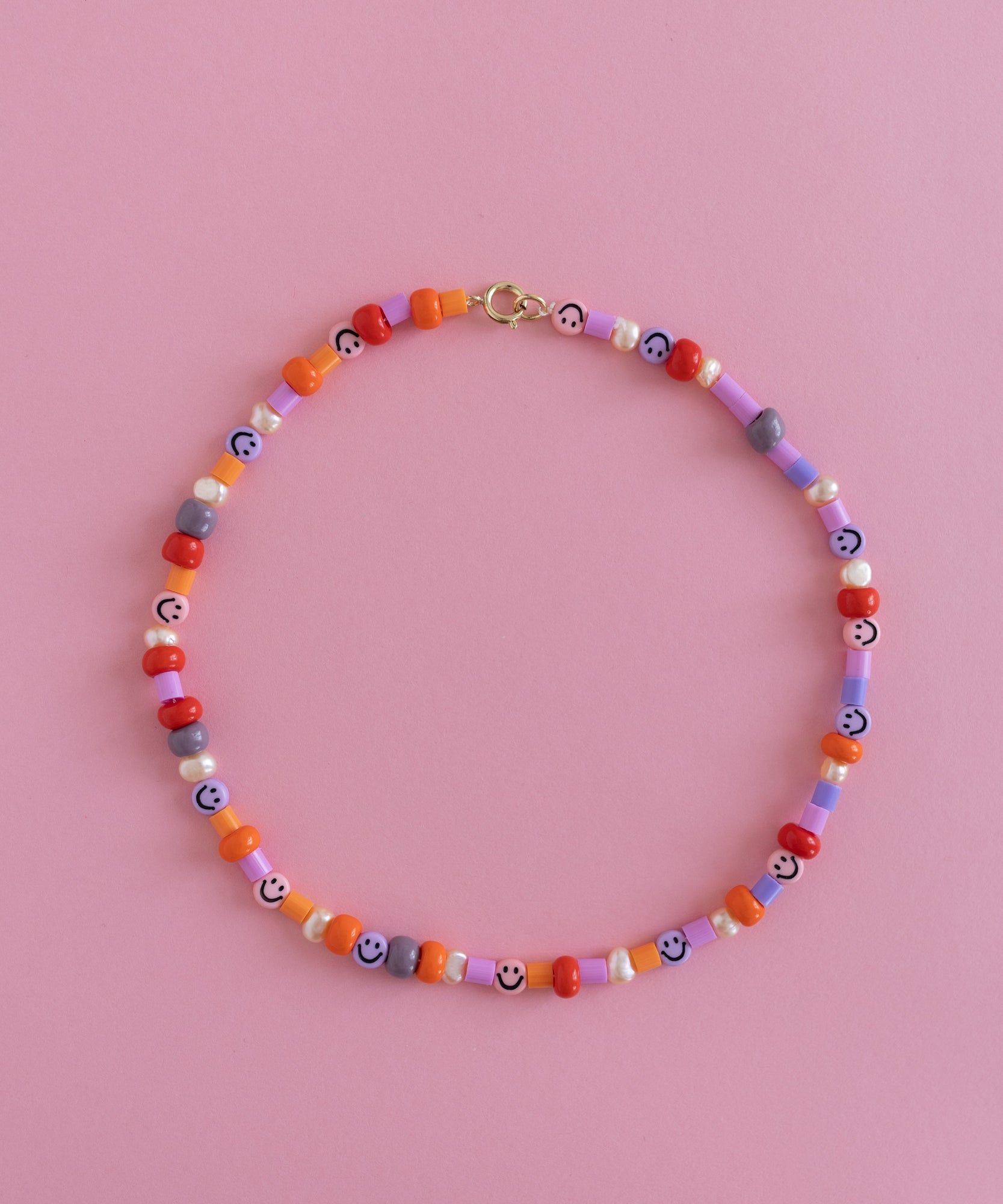 A Candyman Kit beaded necklace with Rose Orange Tones charm on a pink background by WALD World.
