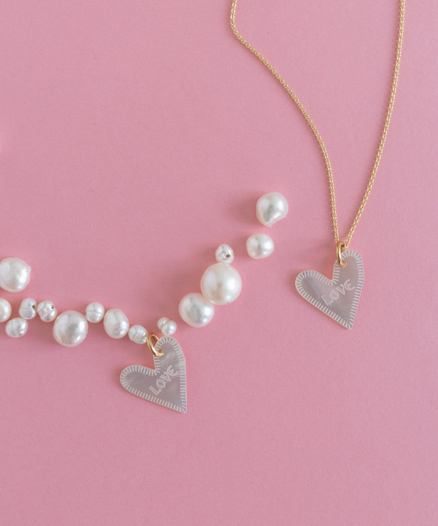 Two Heart Charm Love Cream necklaces with pearls on a pink background by WALD World.