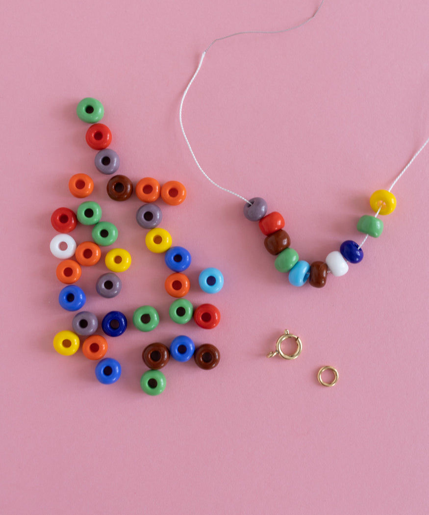 A DIY jewelry kit featuring colorful beads and a ring on a pink background.