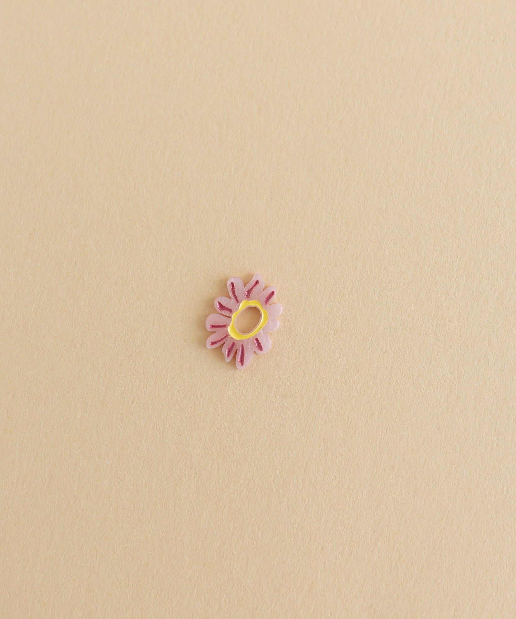 A small Daisy Charm Rose flower jewelry on a beige surface.