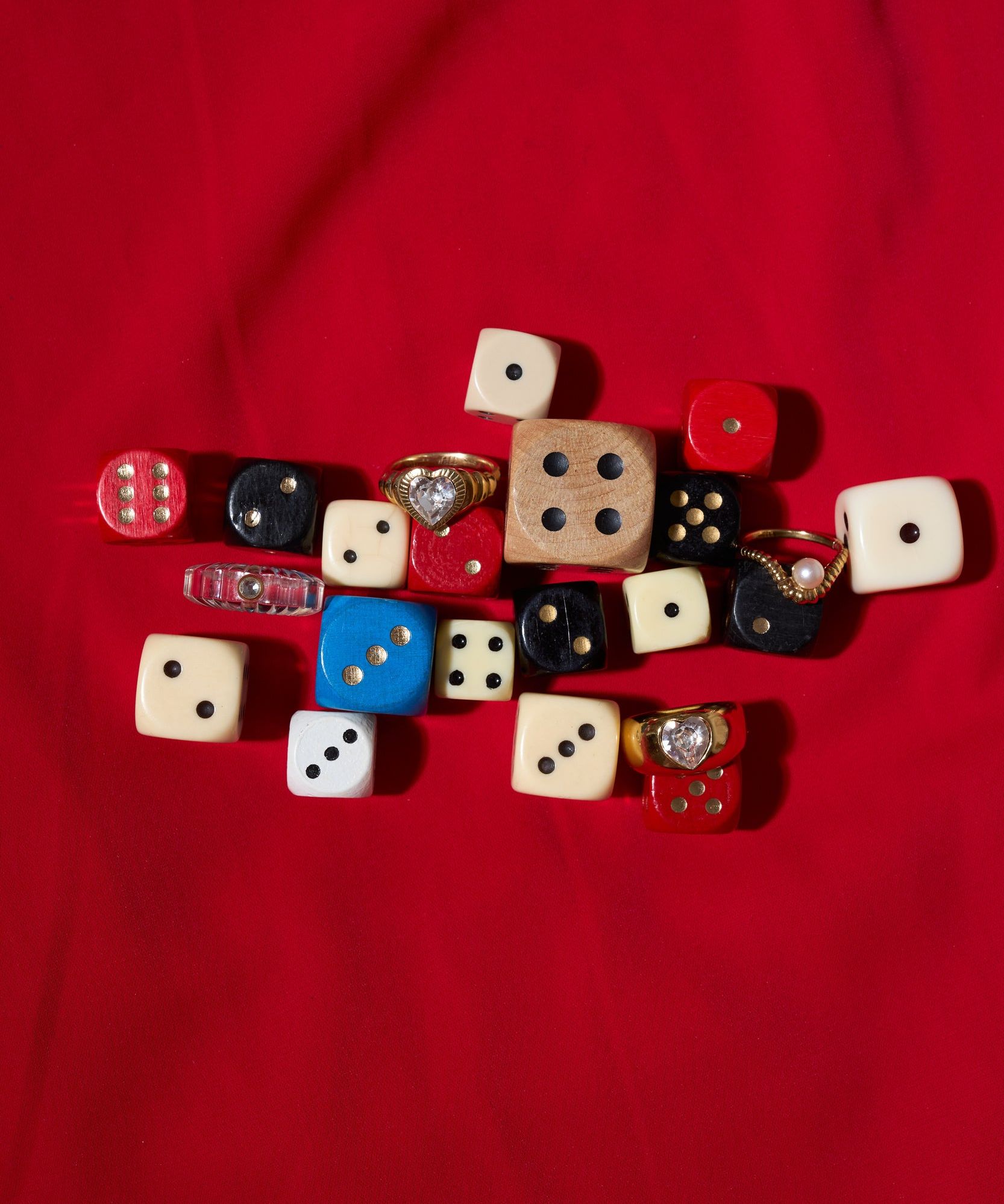 A mix of colorful dice in different sizes, some topped with WALD Berlin’s NYC If I Rule The World Ring, handmade from recycled gold in Germany, displayed on a red fabric background.