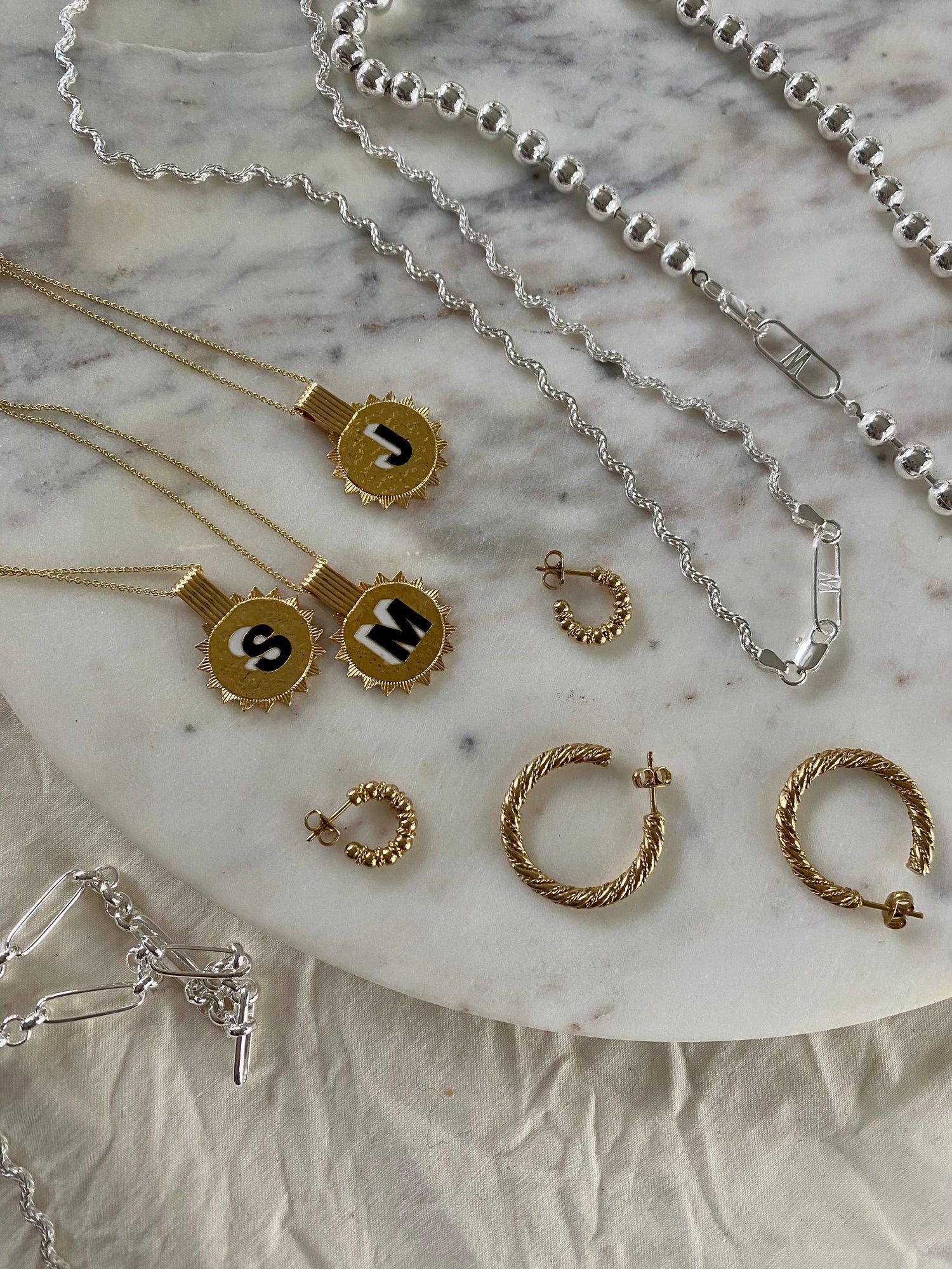 A collection of gold and silver jewelry, including necklaces and WALD Berlin Harry Bracelet Silver, on a marble table.