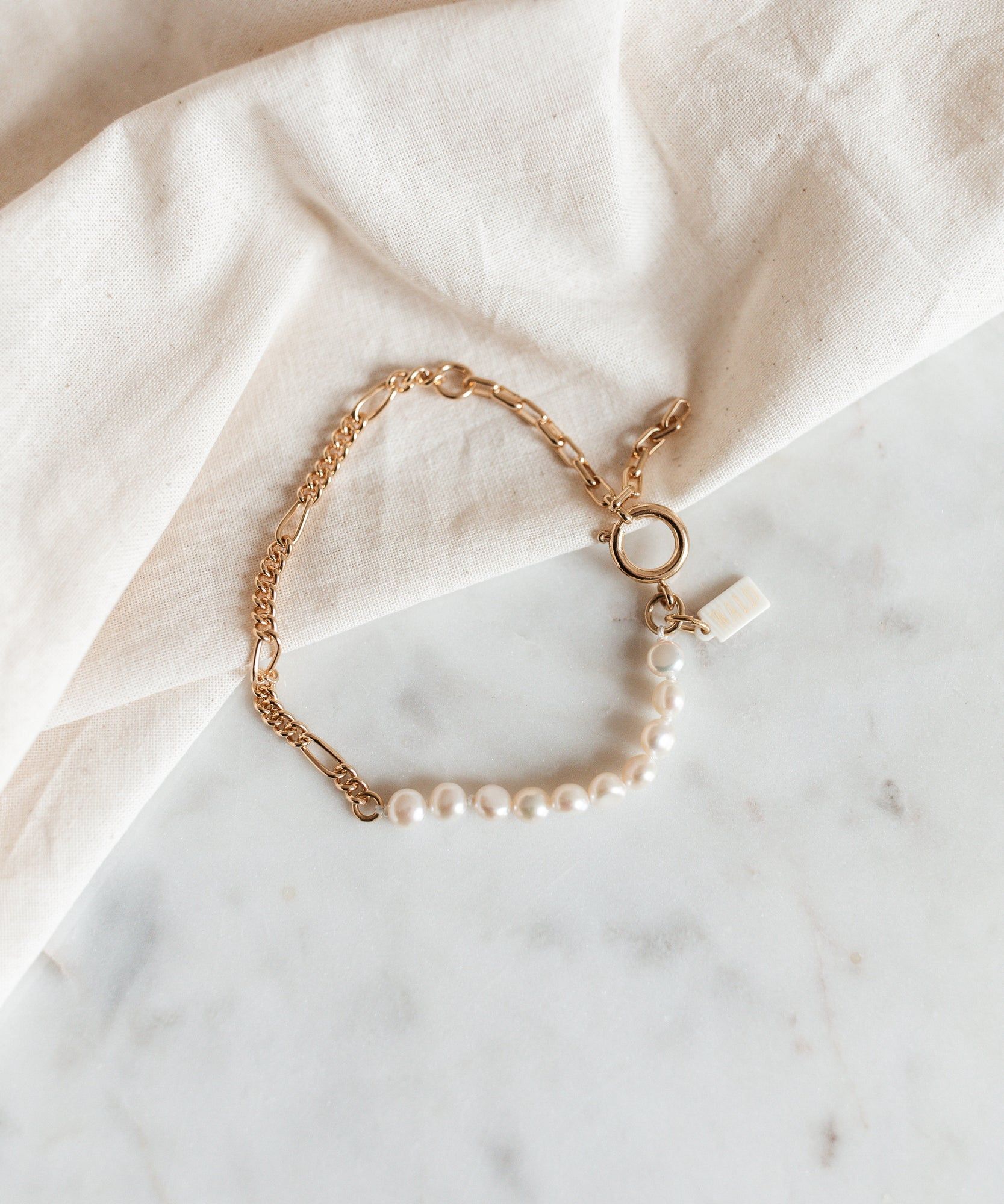 A WALD Berlin Pas De Deux Bracelet with a gold chain on a marble table.