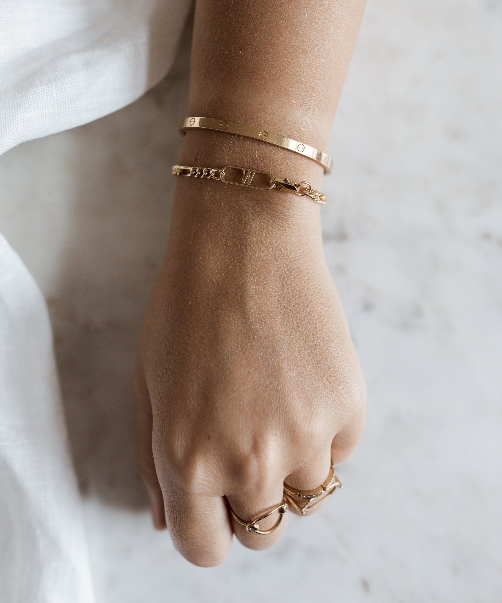 A woman's hand with two WALD Berlin Naomi Gold Bracelets and a gold ring.