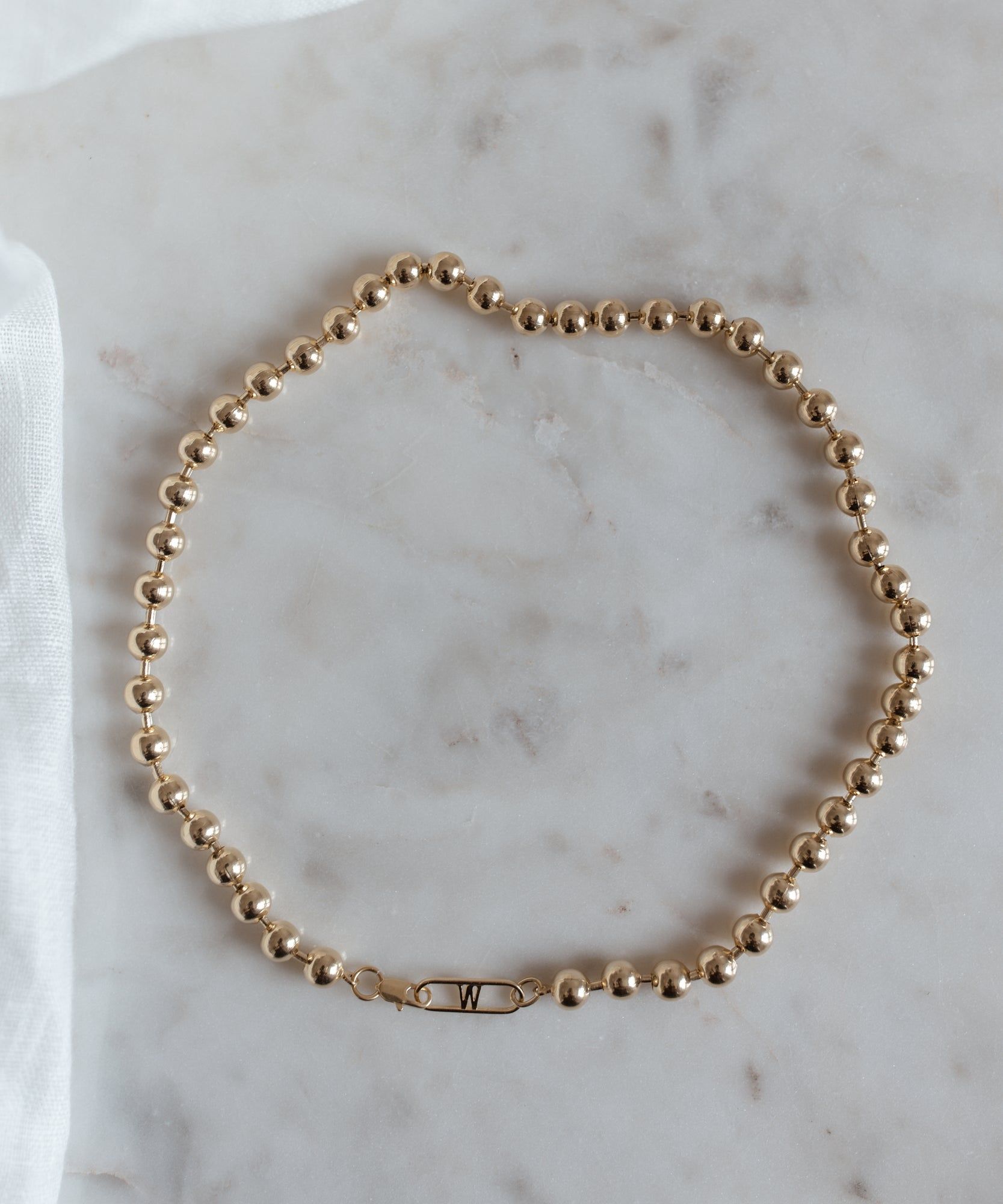 An WALD Berlin Harry Necklace Gold beaded choker on a white table.