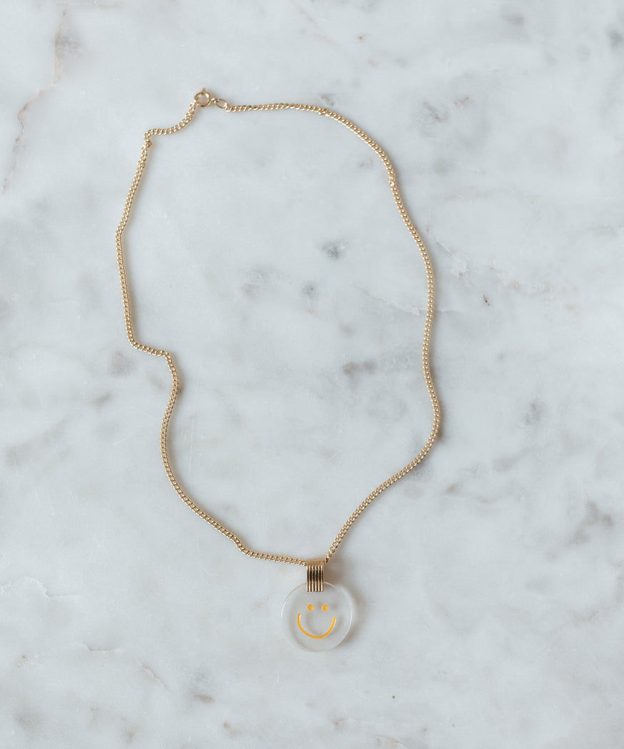 A Smilie Dude Medaillon Gold Necklace from WALD Berlin, a German jewelry brand, with a white circle on it.