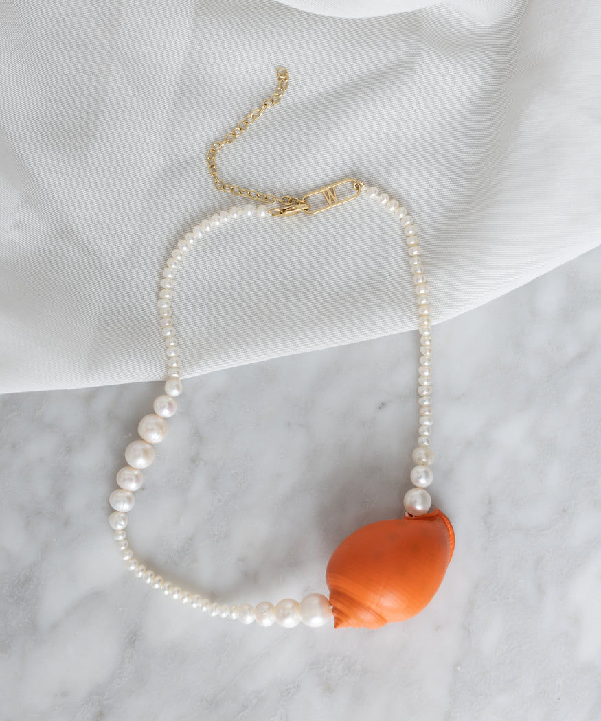 A WALD Berlin La Piscina Juicy Pearl Necklace Orange is displayed on a light fabric background, featuring an adjustable length for the perfect fit.