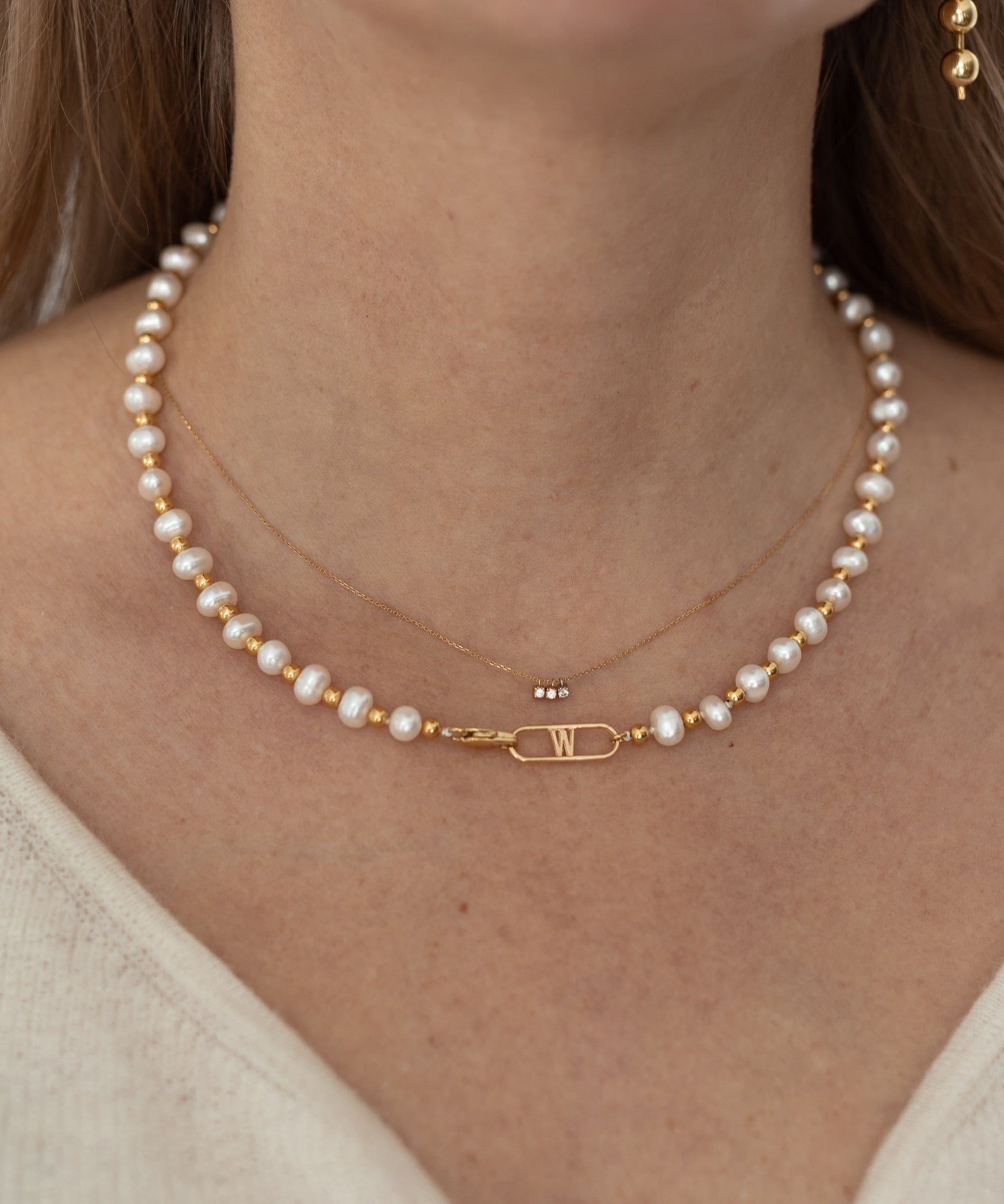 A woman adorned with a WALD Berlin NYC Paris Paris Necklace featuring pearls and a dainty gold chain.