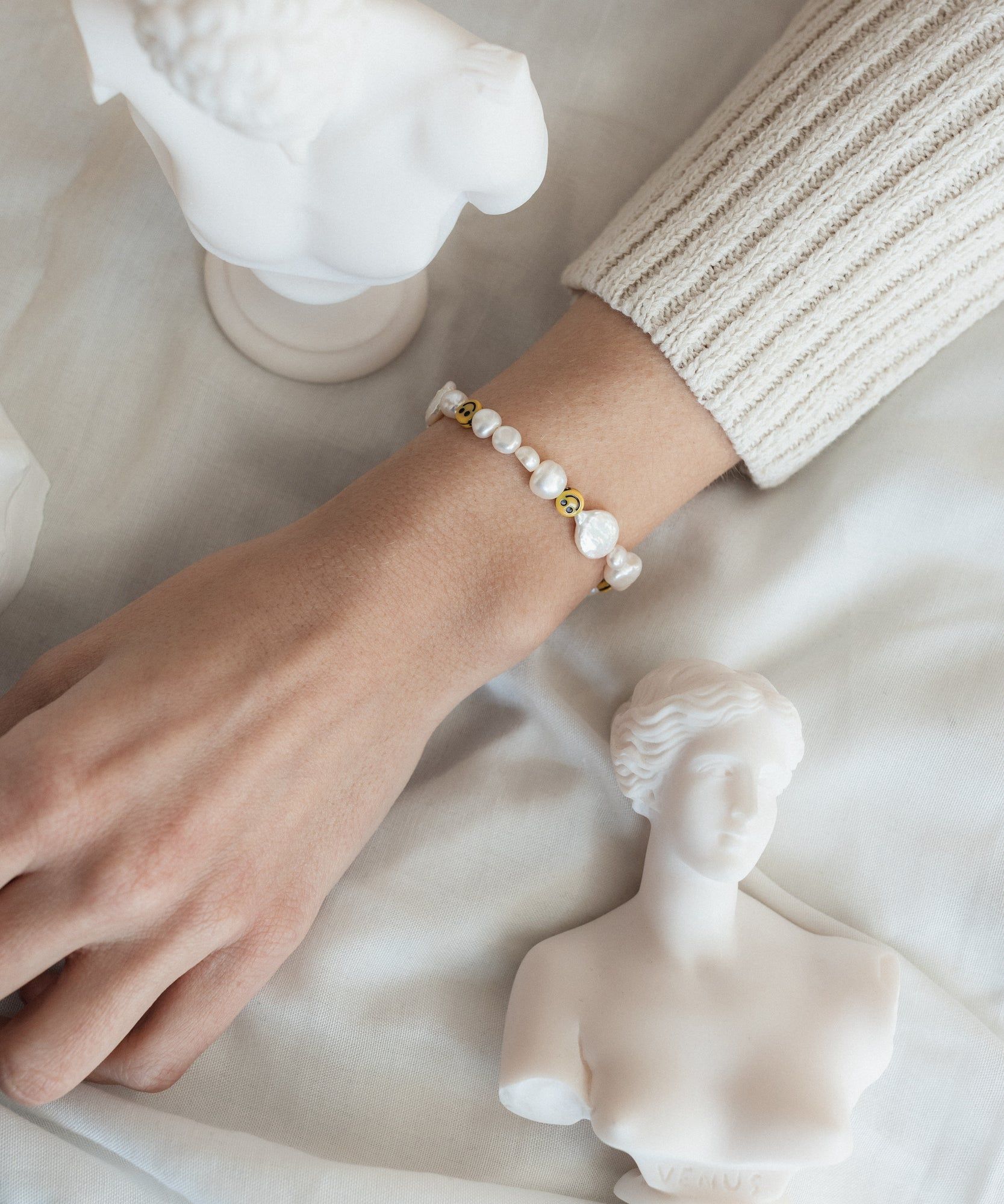 A woman's hand wearing a WALD Berlin Smilie Dude Pearl Bracelet with Extention beside a statue in Berlin, Germany.