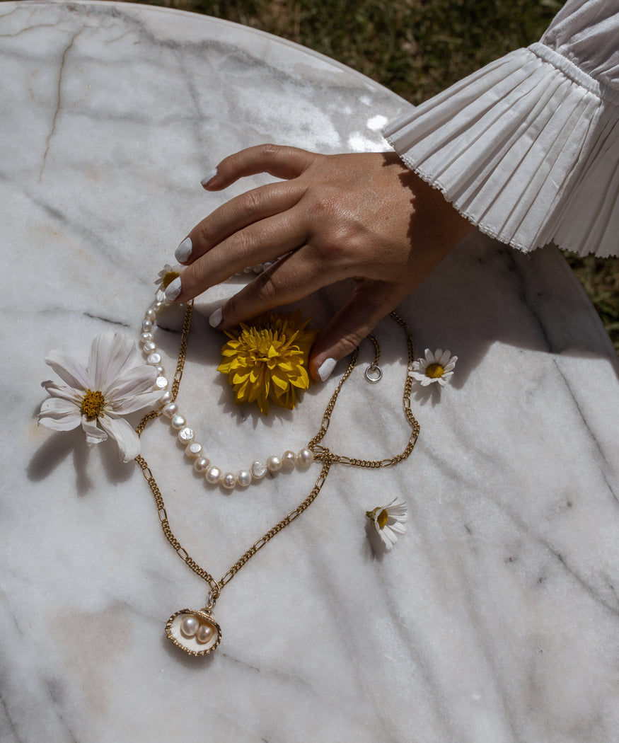 A woman's hand holding a WALD Berlin €25 Gift Card with pearls and daisies on a marble table in Germany.