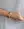 A wrist adorned with two braided bracelets featuring smiley face beads and a gold metal bracelet includes the Smilie Dude Pink Friendship Bracelet by WALD Berlin.