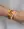 A wrist adorned with WALD Berlin's Smilie Dude Orange Friendship Bracelet alongside two other colorful braided string bracelets featuring smiley face beads, paired with a single gold metal bracelet.