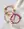 The WALD Berlin Smilie Dude Orange Friendship Bracelet, along with red and pink woven rope bracelets featuring small yellow smiley face charms, are displayed on a light fabric background.