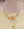 A person wears a yellow textured garment with layered necklaces, including beaded 18k gold plated pieces and WALD Berlin's Pop Smilie Mini necklace featuring a green Smilie Medaillon pendant.